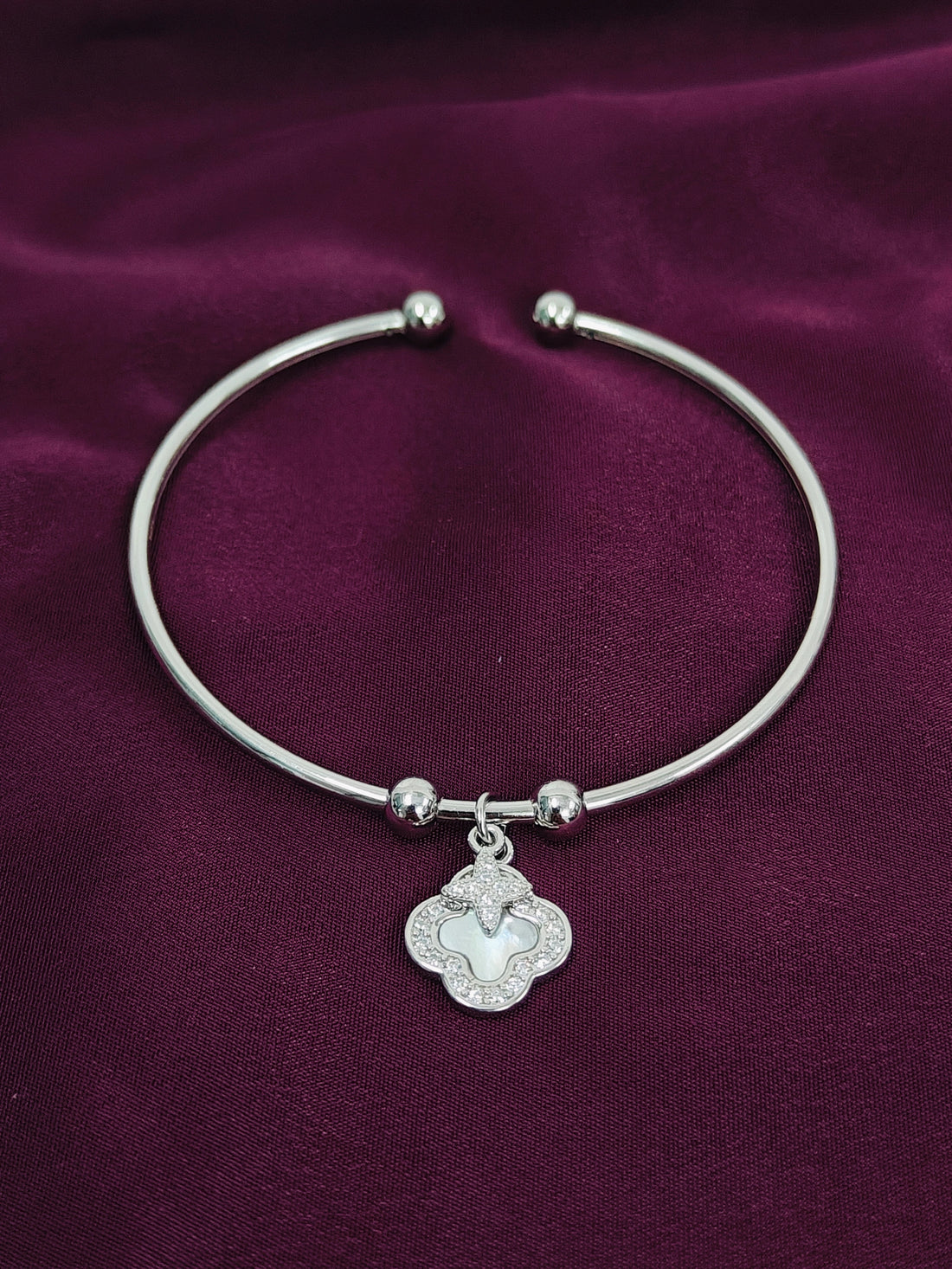 Silver bracelet with a clover-shaped charm on a purple fabric background