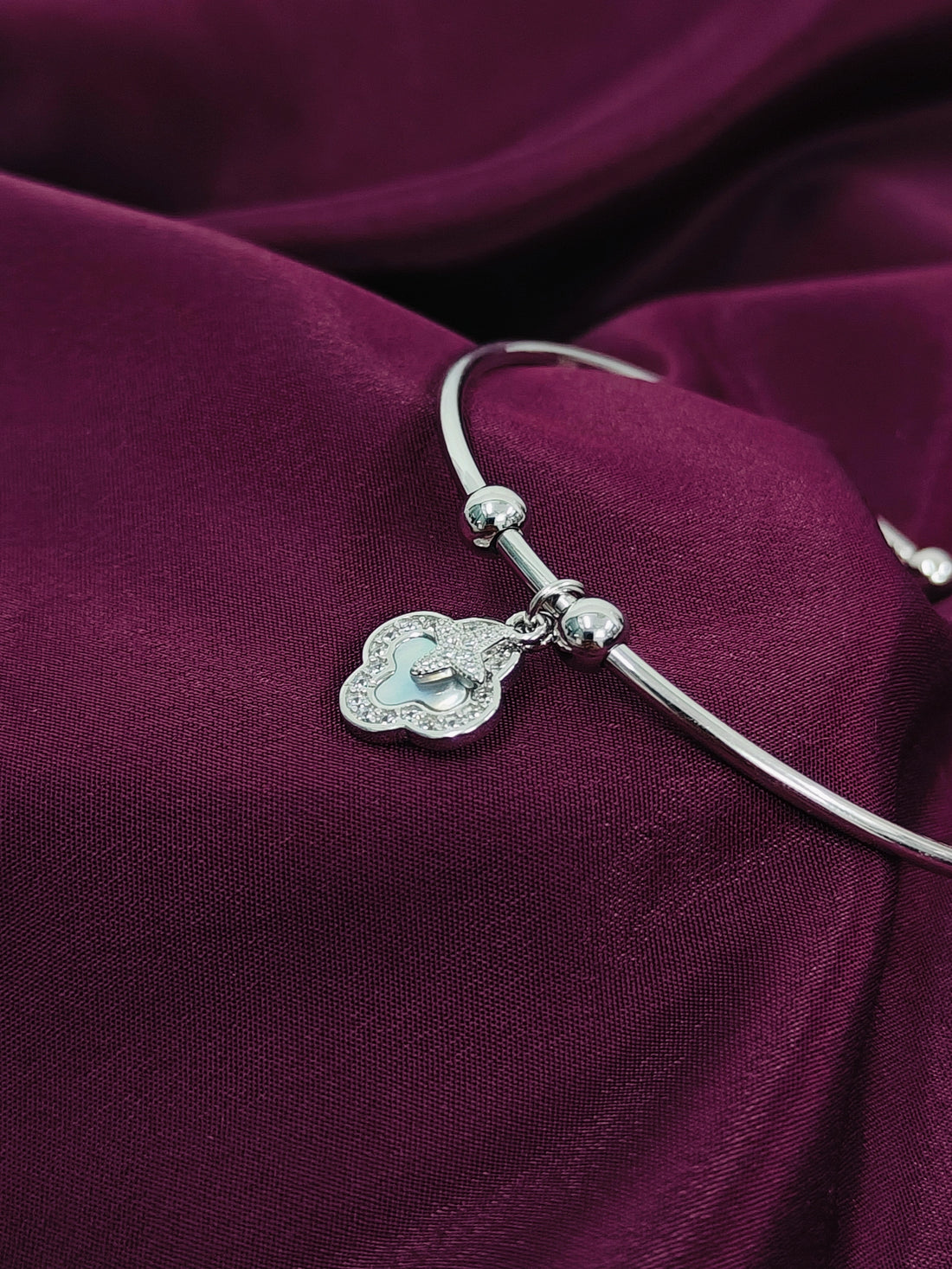 Silver bracelet with a heart-shaped charm on a purple fabric background