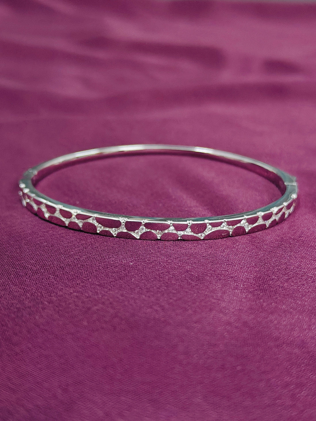 Silver bracelet with red pattern on a purple fabric background