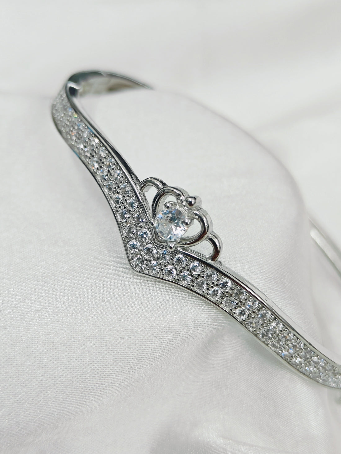 Silver bracelet with heart-shaped clasp and clear stones on a white background