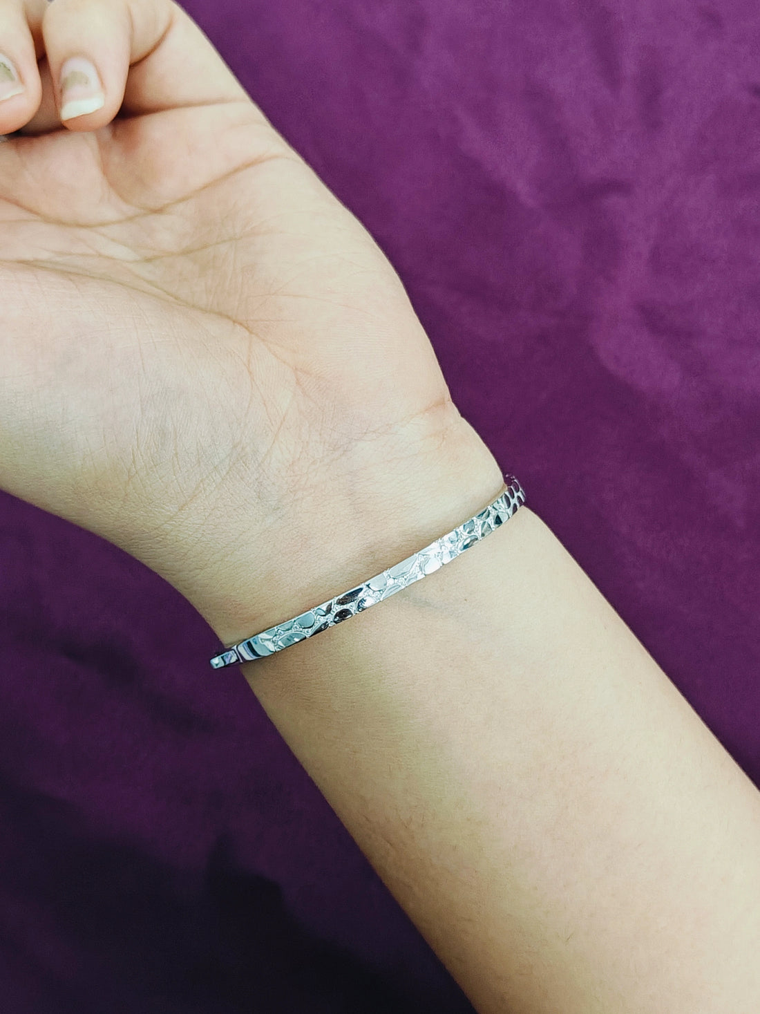 Silver bracelet on a wrist against a purple background