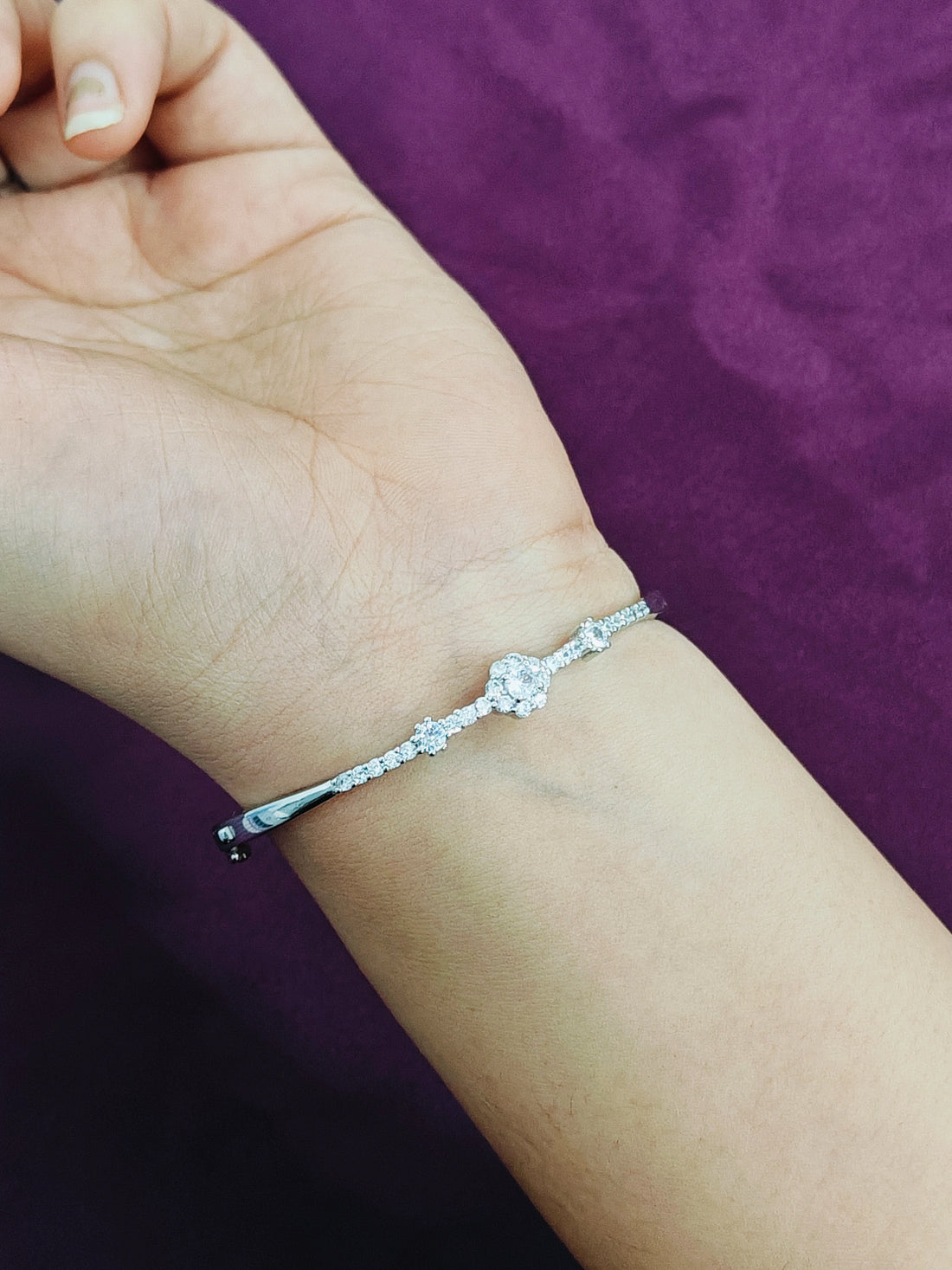 Silver bracelet on a wrist with a purple background