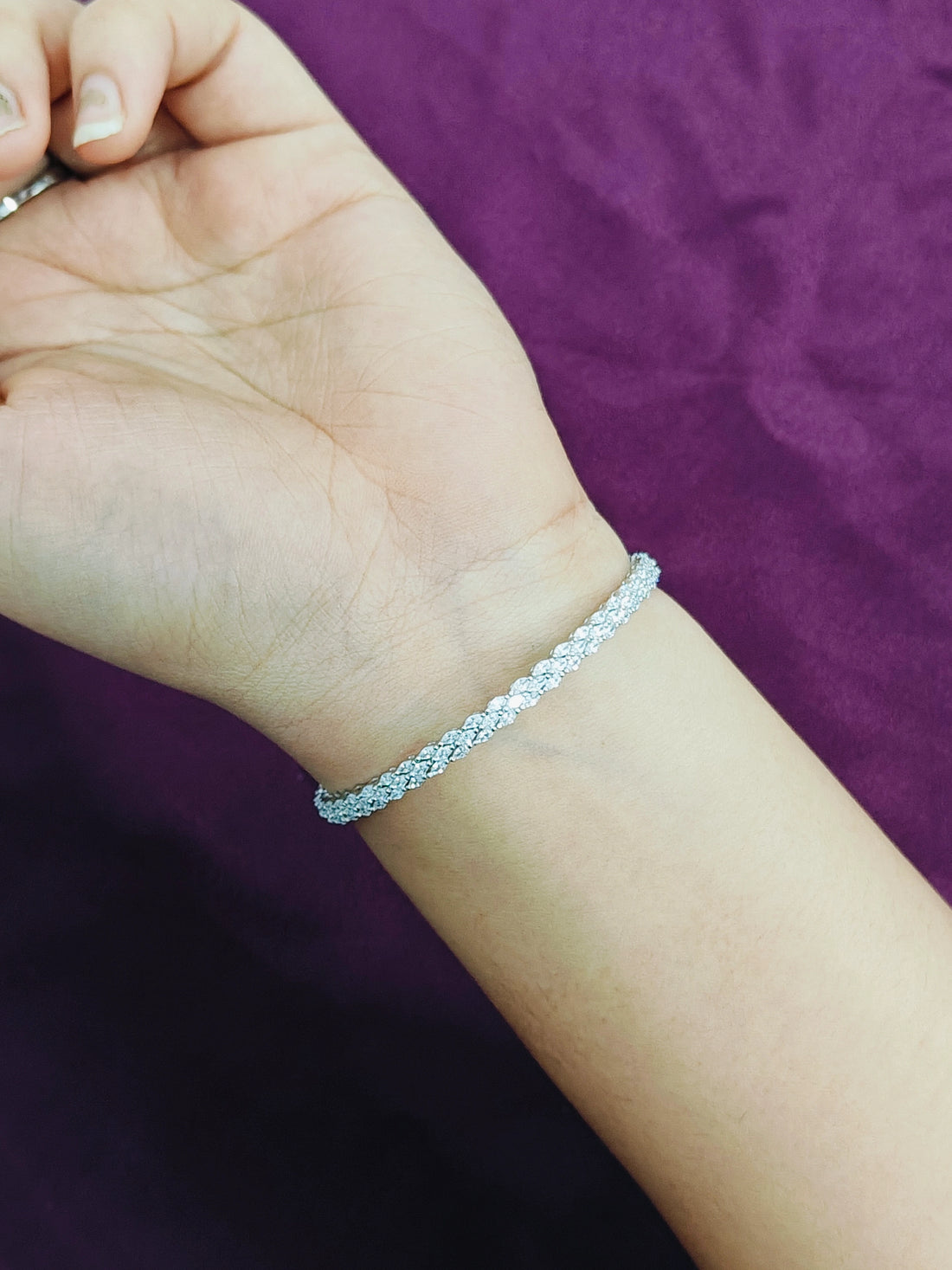 Silver bracelet on a wrist with a purple fabric background
