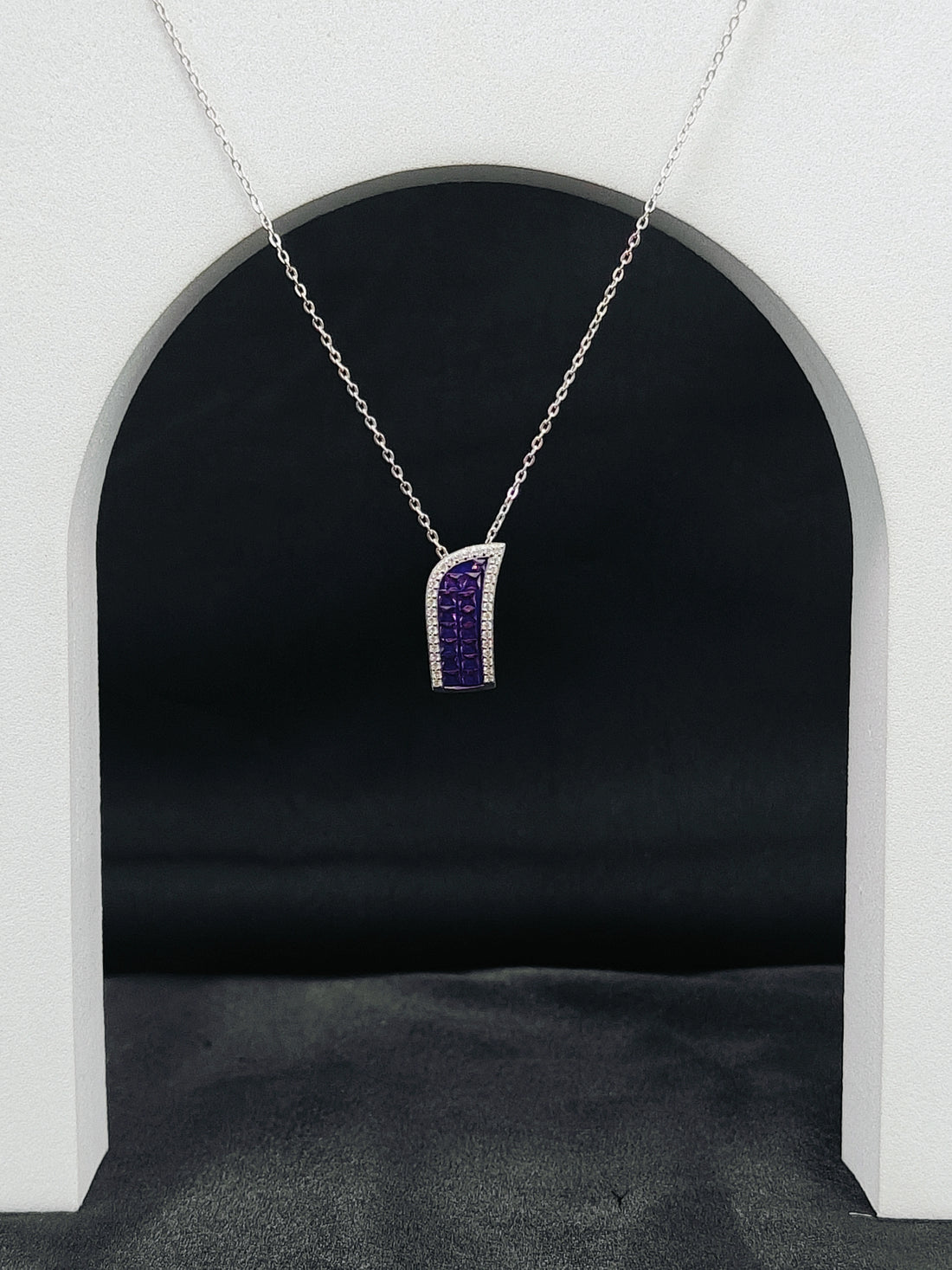 Silver necklace with a purple pendant hanging against a black background