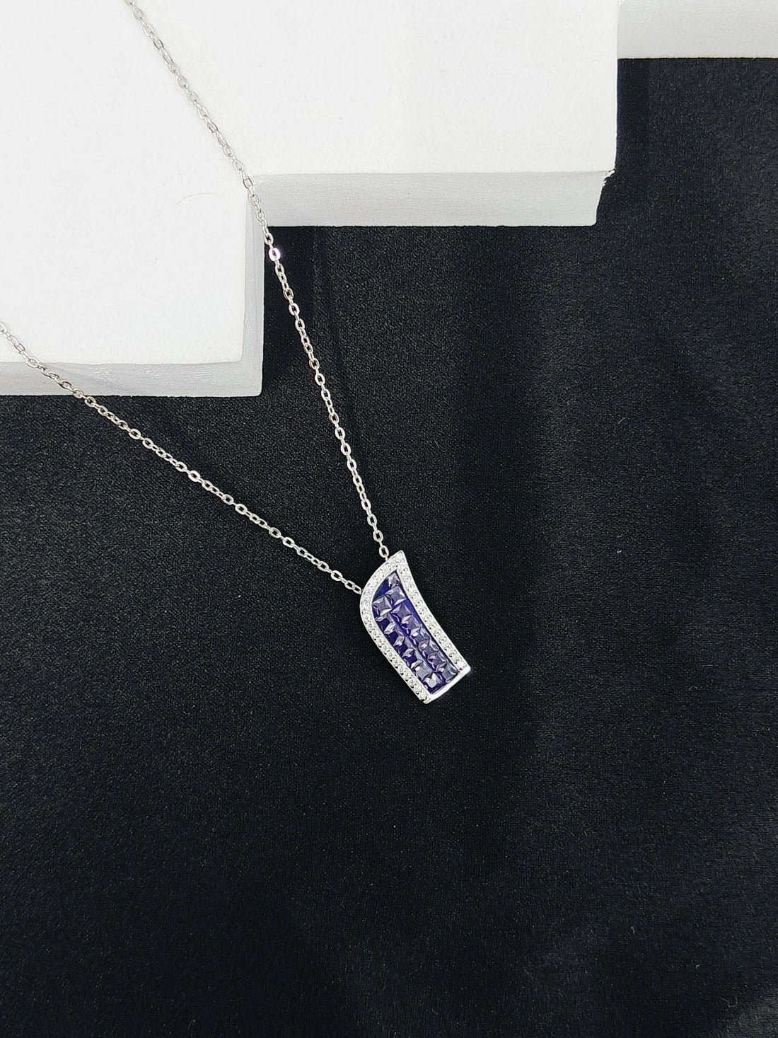 Silver necklace with a purple pendant on a black background