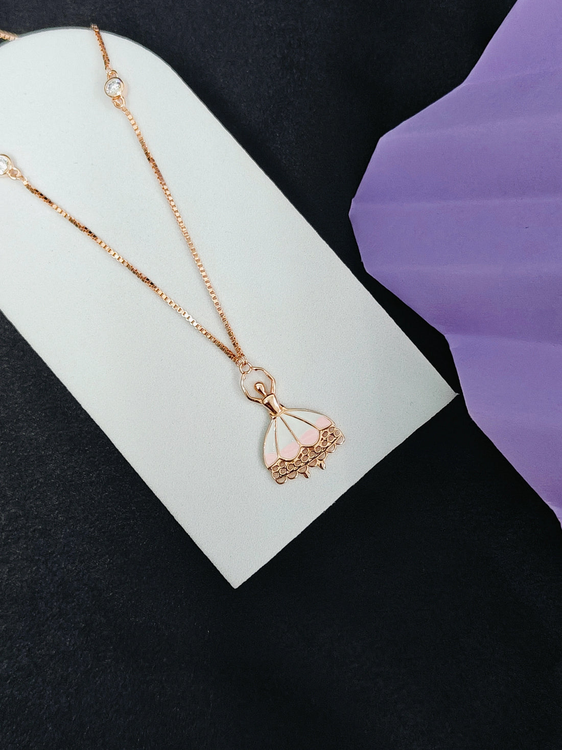Rose gold necklace with a delicate pendant on a white card against a black background