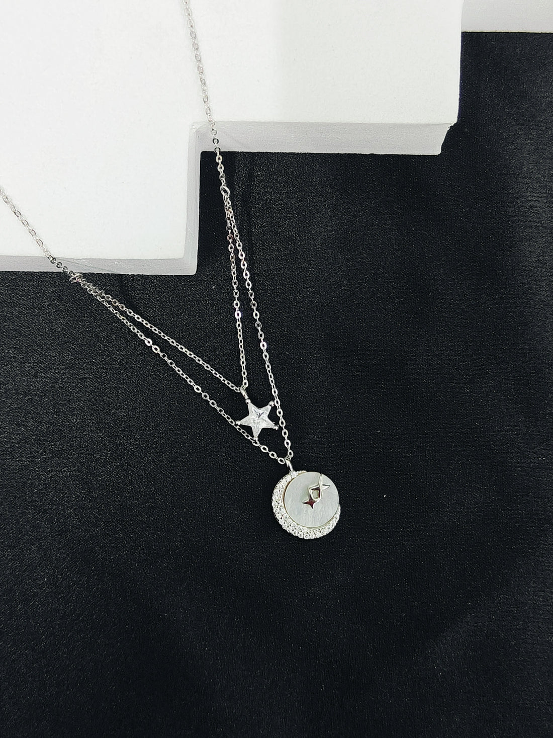 Silver necklace with star and round pendant on a black surface