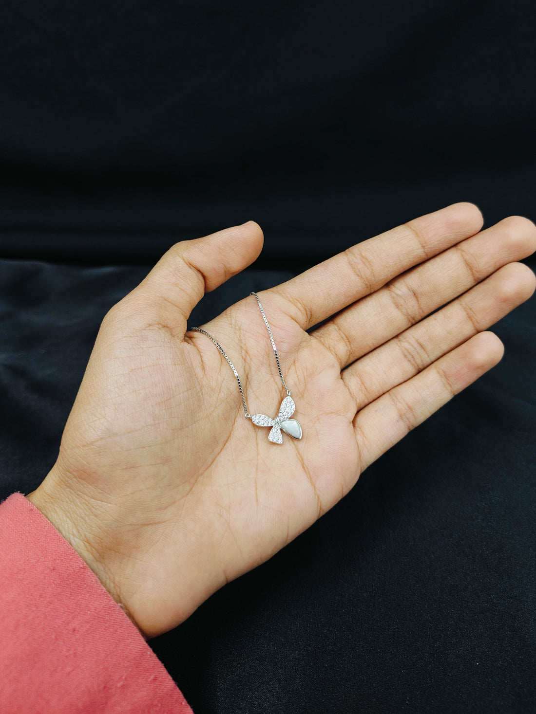 Hand holding a delicate silver necklace against a black background