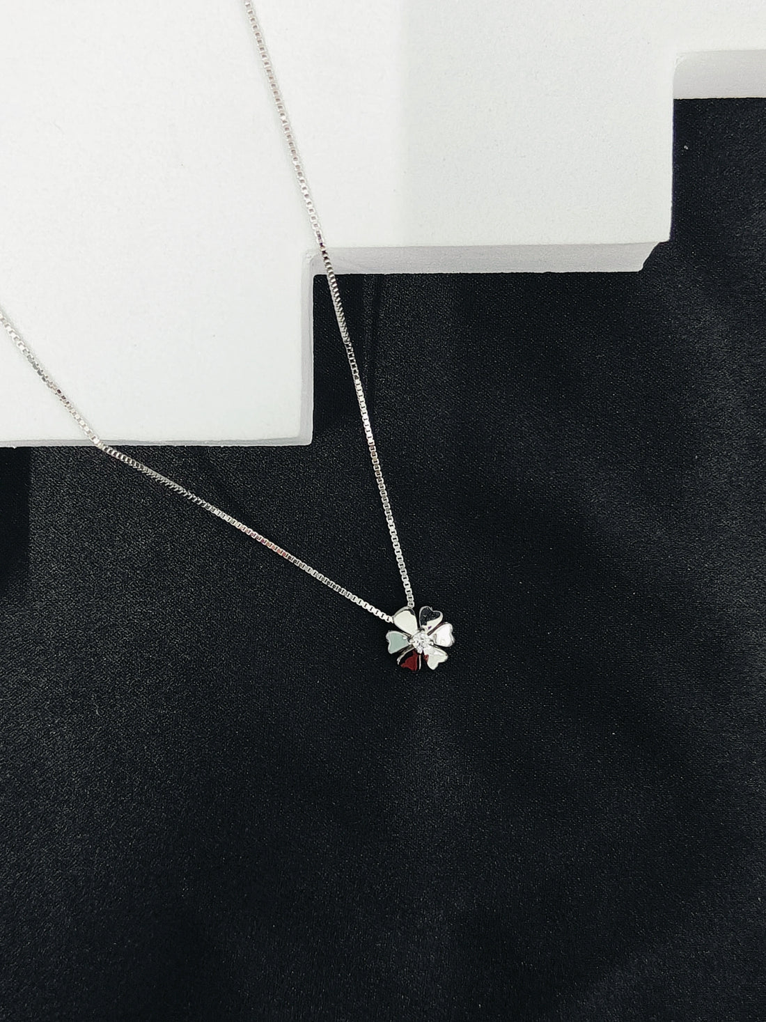 Silver necklace with a clover pendant on a black surface