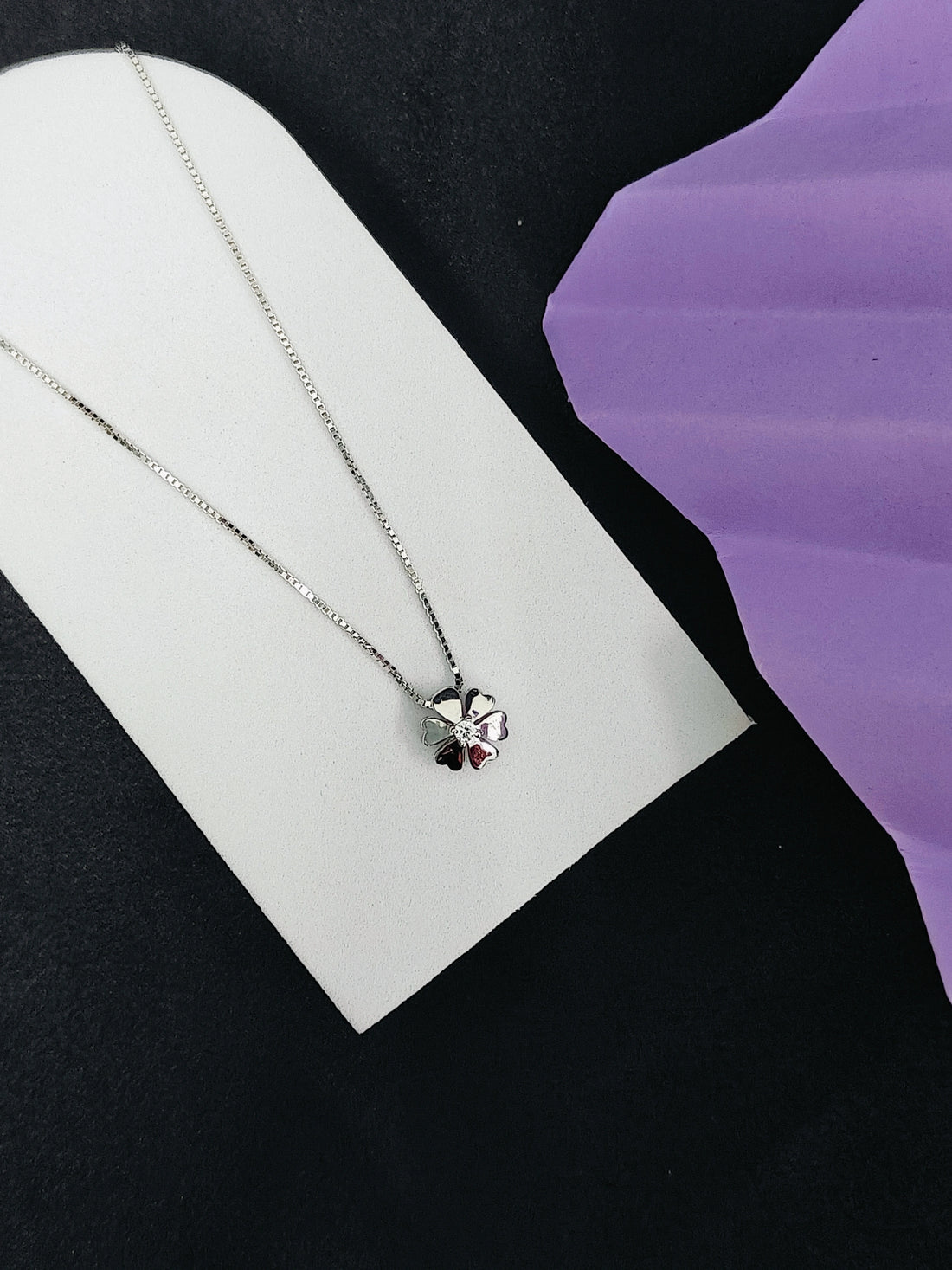 Silver necklace with a heart pendant on a white card against a black and purple background