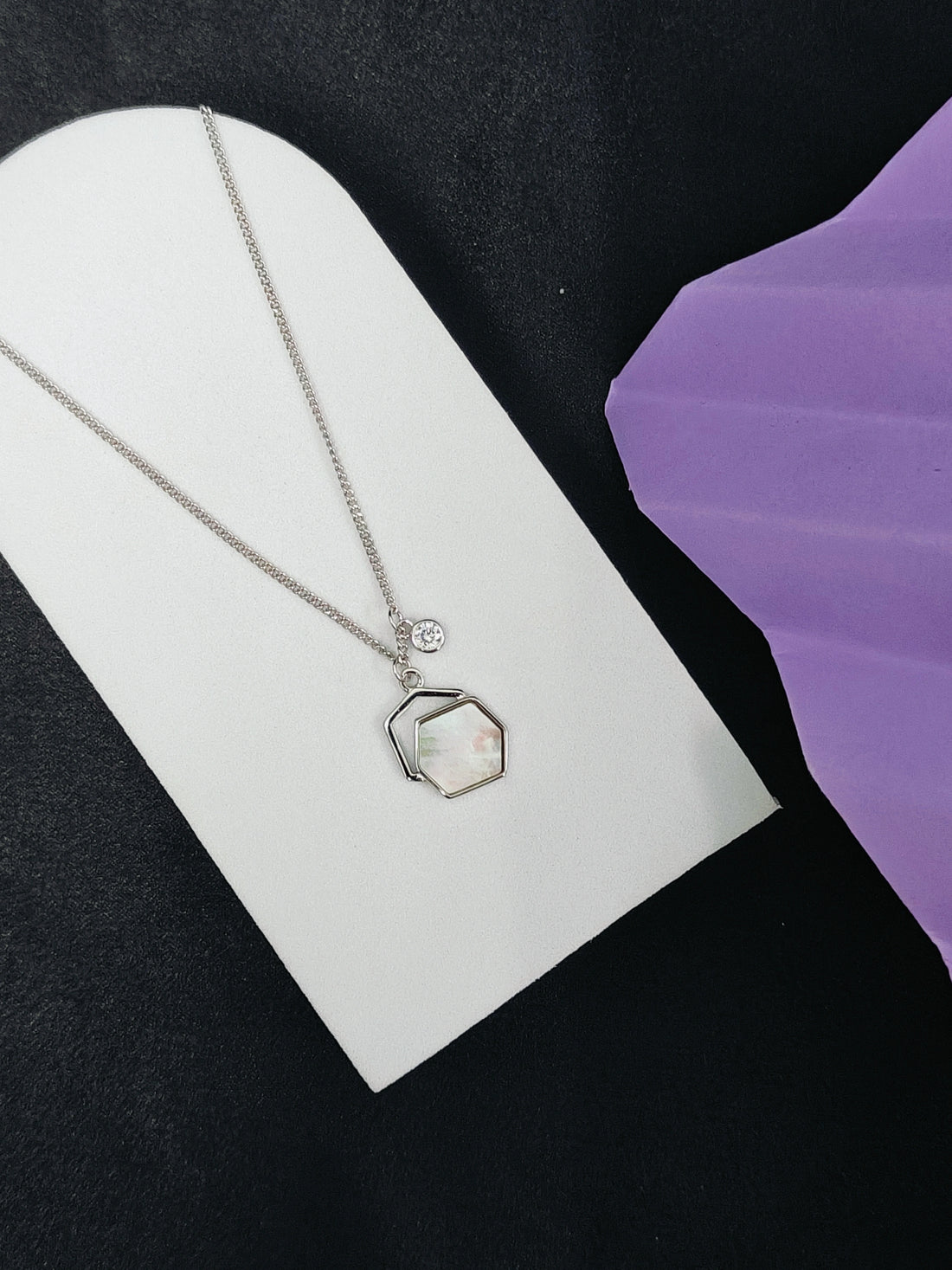 Silver necklace with a hexagonal pendant on a white card against a black and purple background