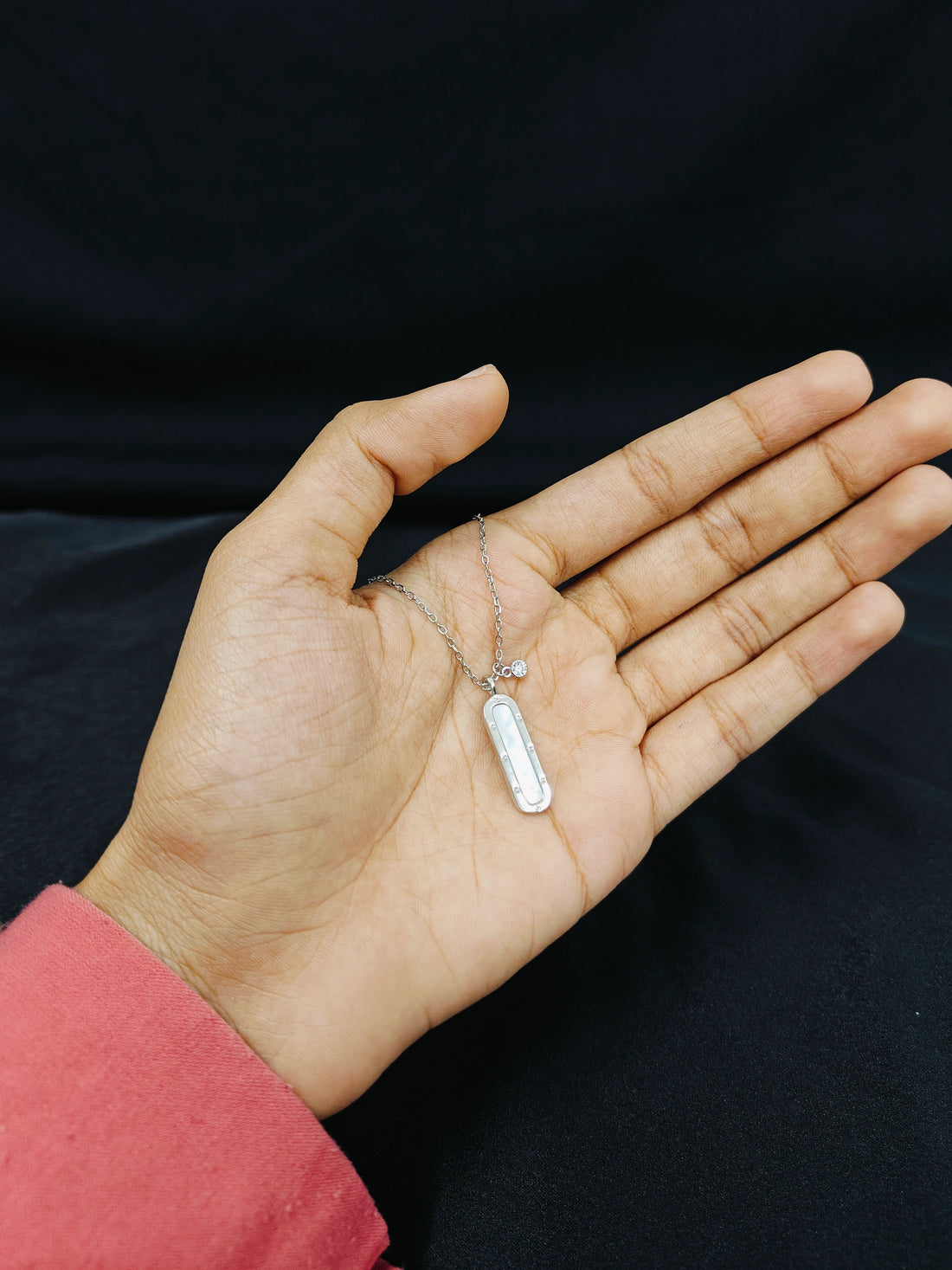 Hand holding a silver necklace with a tag against a black background