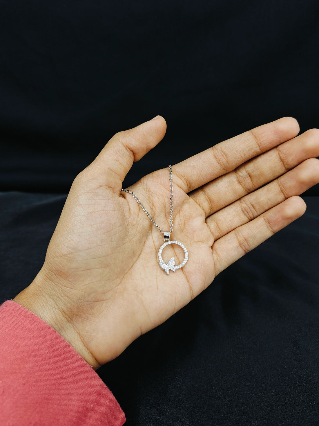 Hand holding a silver necklace with a circular pendant against a black background