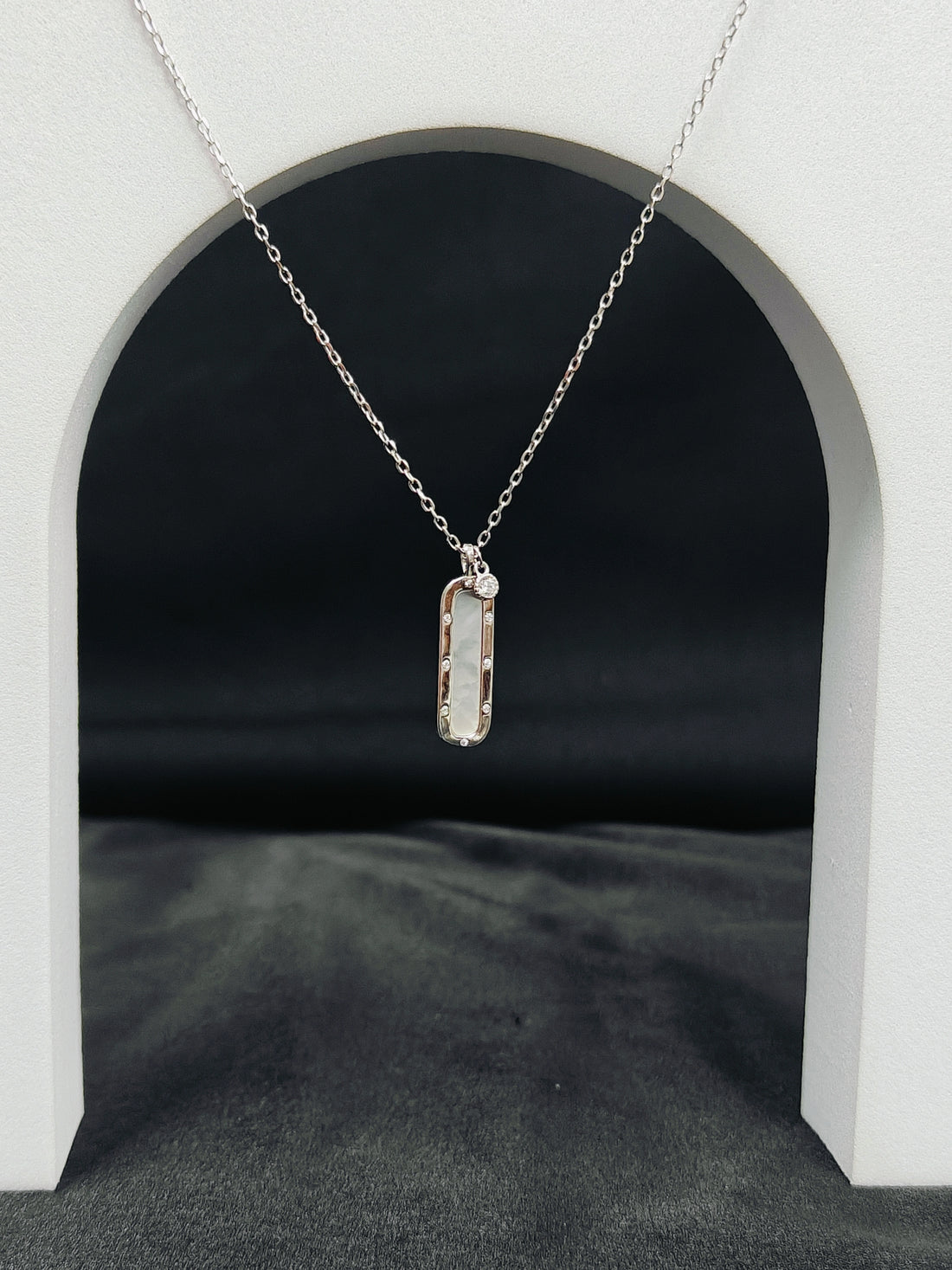 Silver necklace with a rectangular pendant on a black background
