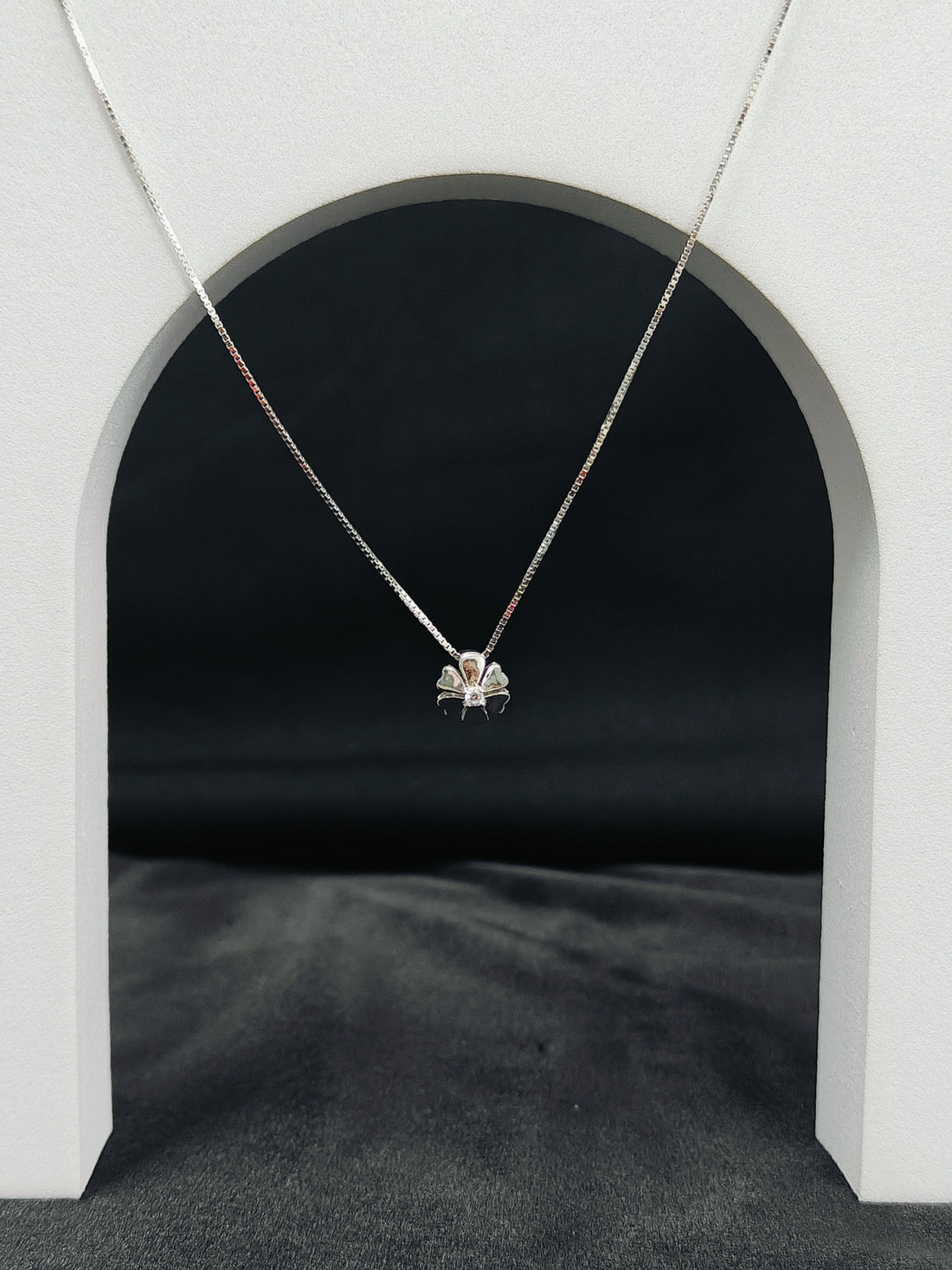 Necklace with a pendant hanging in front of a black archway on a gray surface.