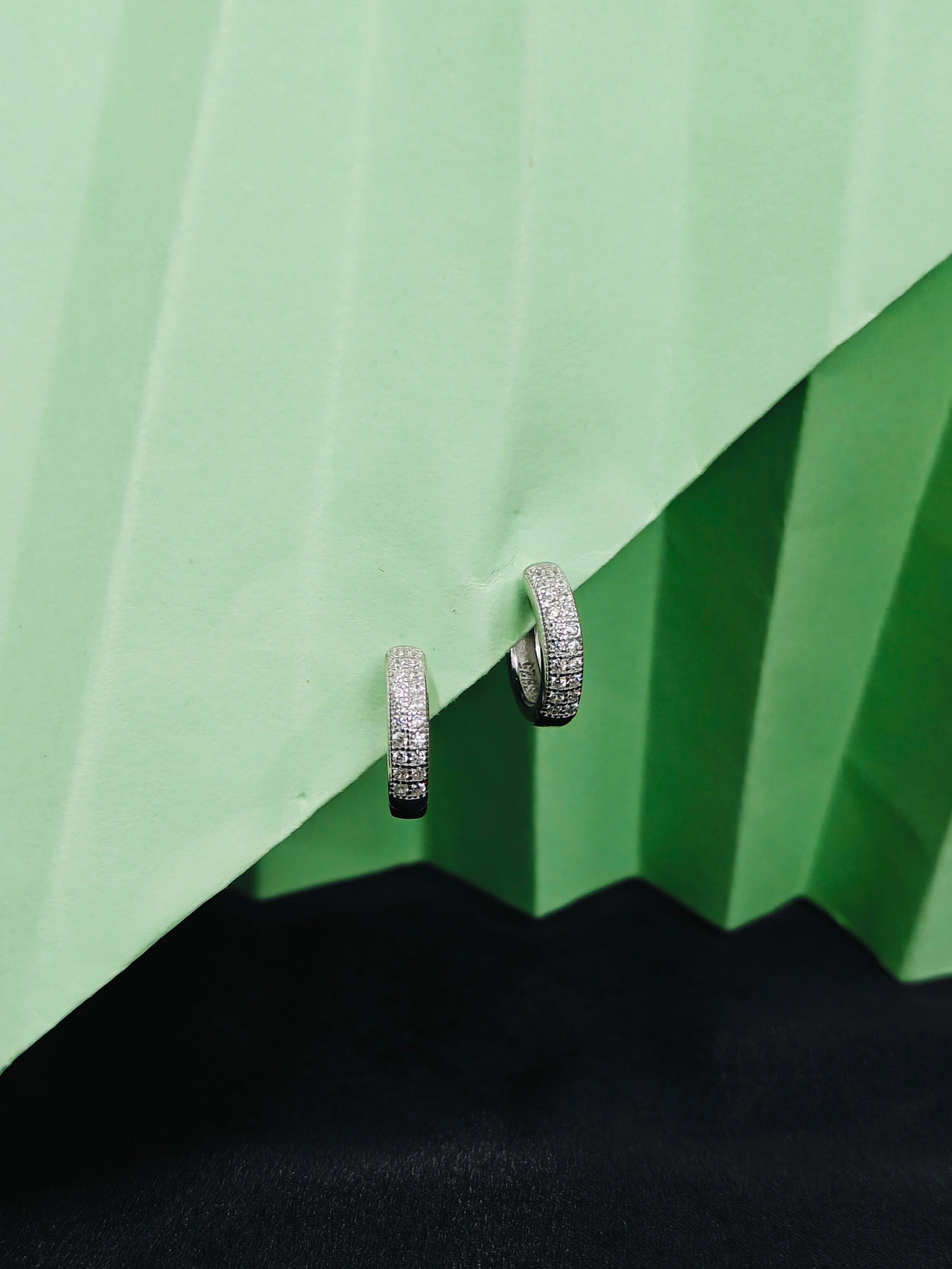 Silver hoop earrings with embedded stones on a green geometric background