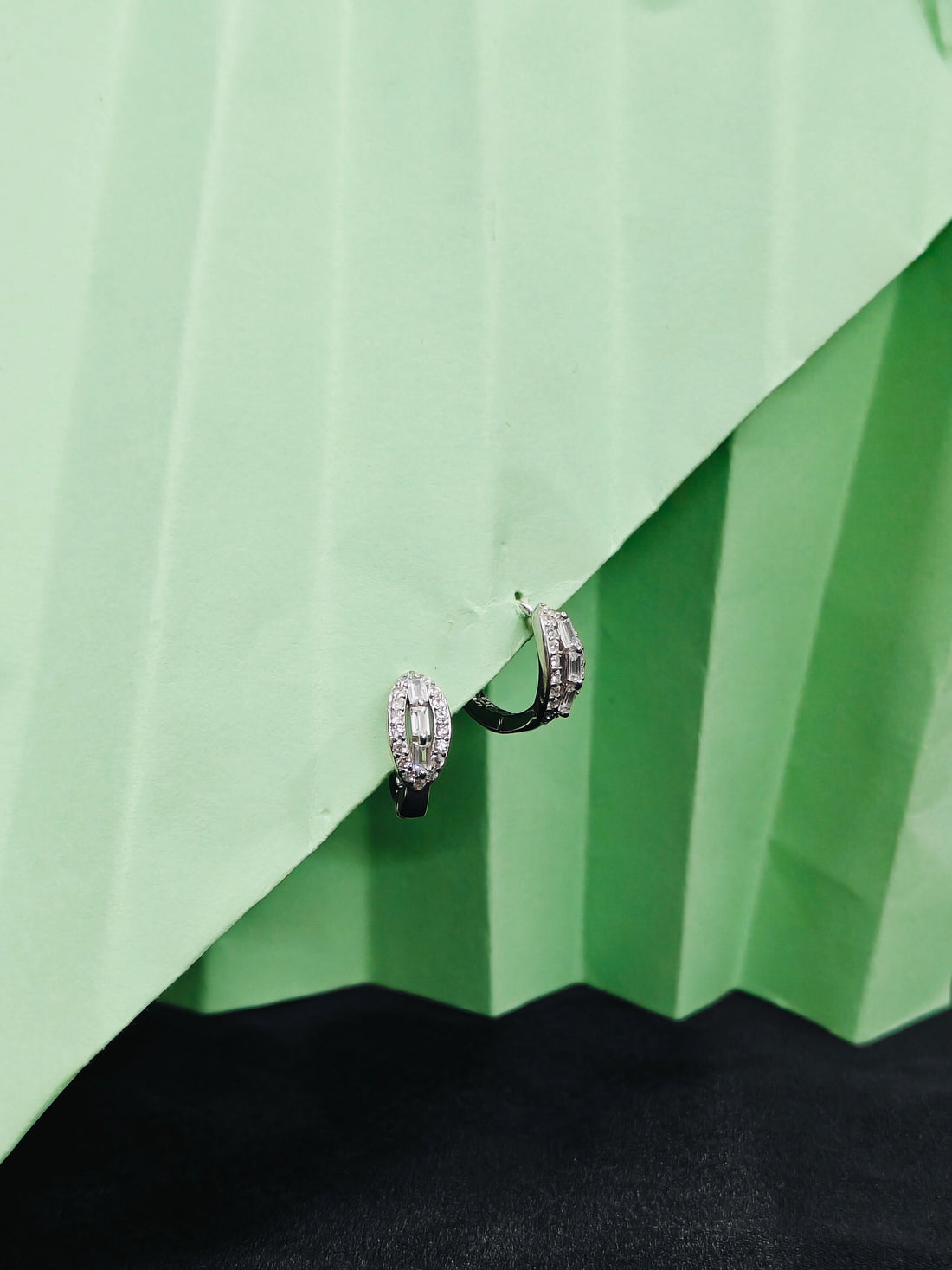 Pair of hoop earrings on a green pleated fabric background