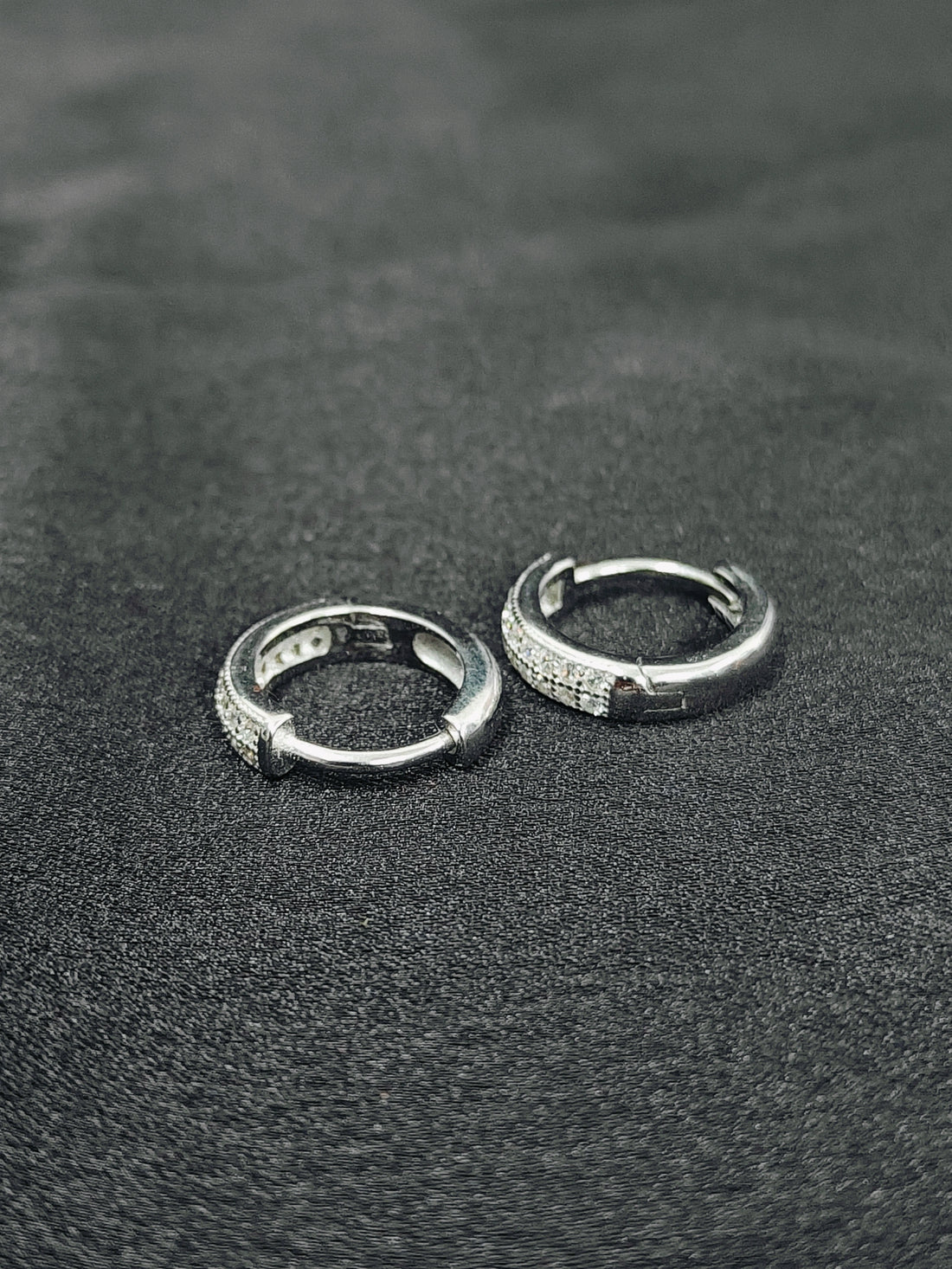 Two silver hoop earrings on a textured black surface