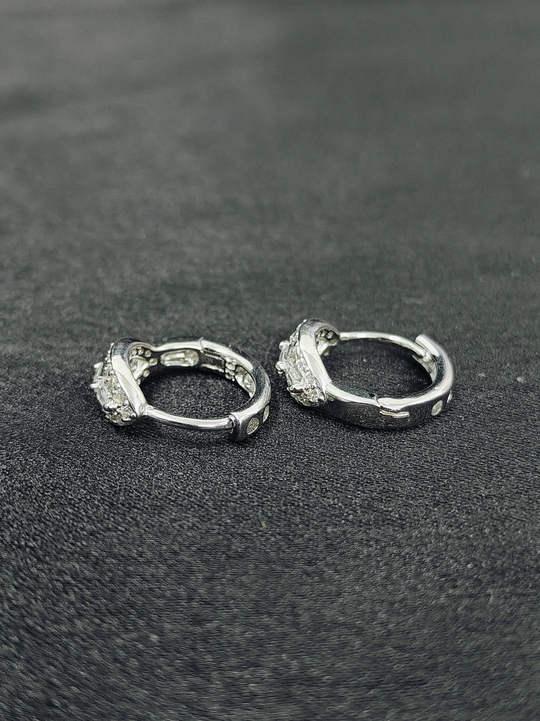 Pair of silver hoop earrings on a textured black surface