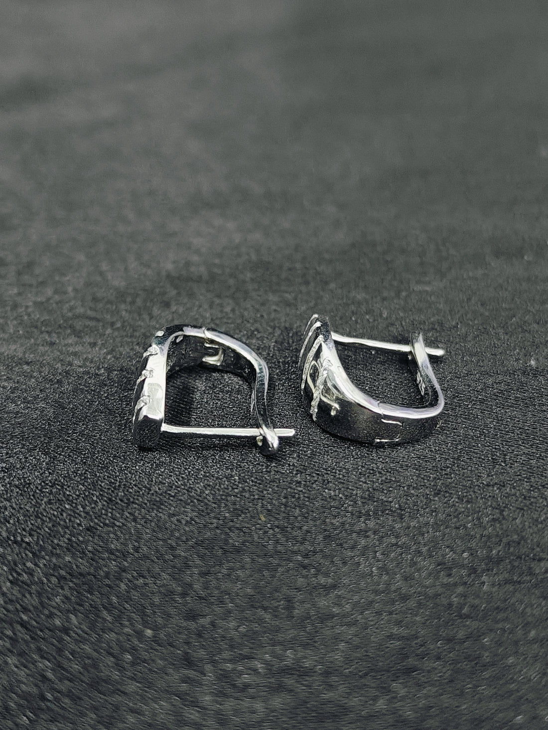 Pair of silver hoop earrings on a black textured surface