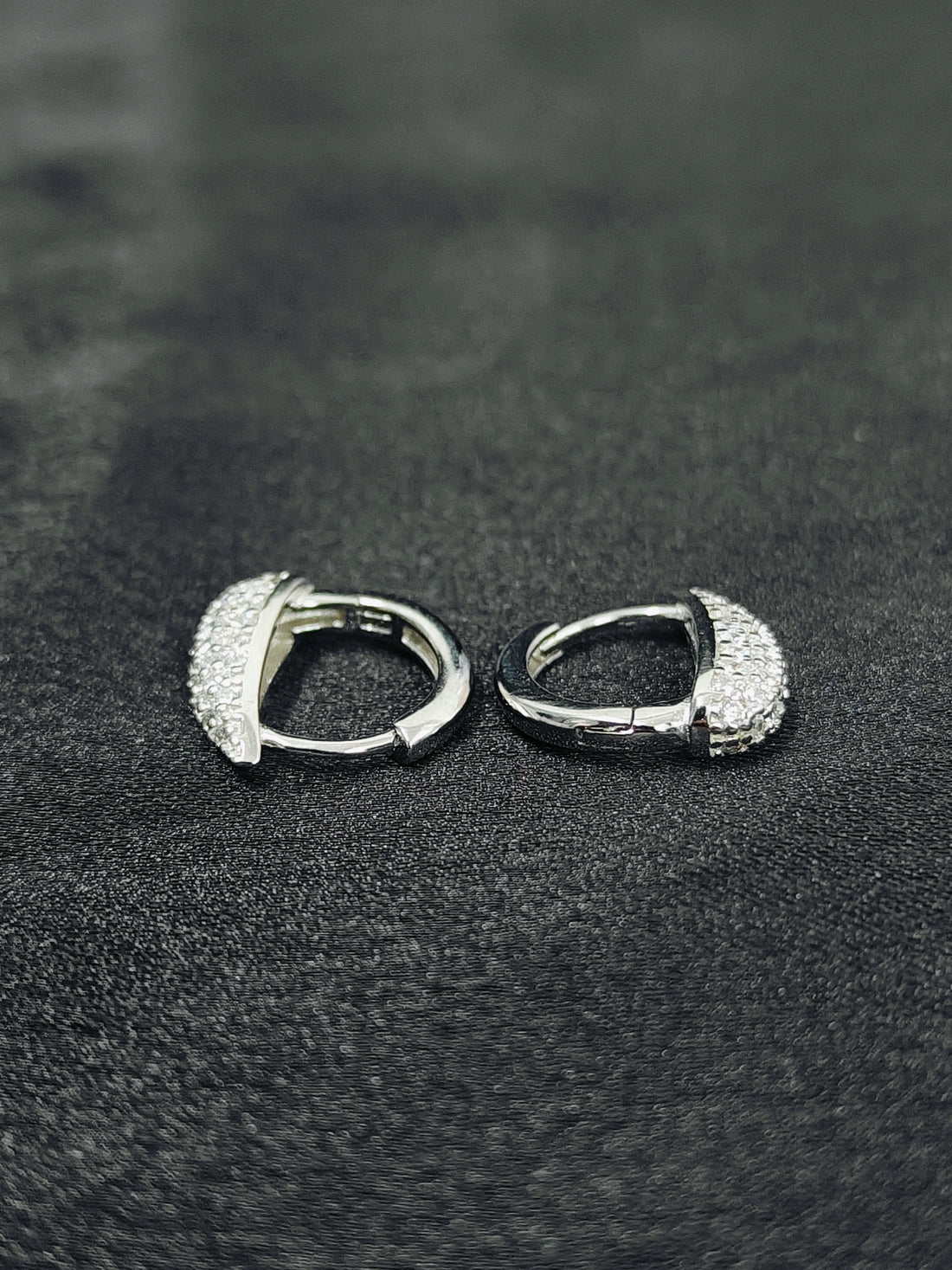 Pair of silver hoop earrings on a black textured surface