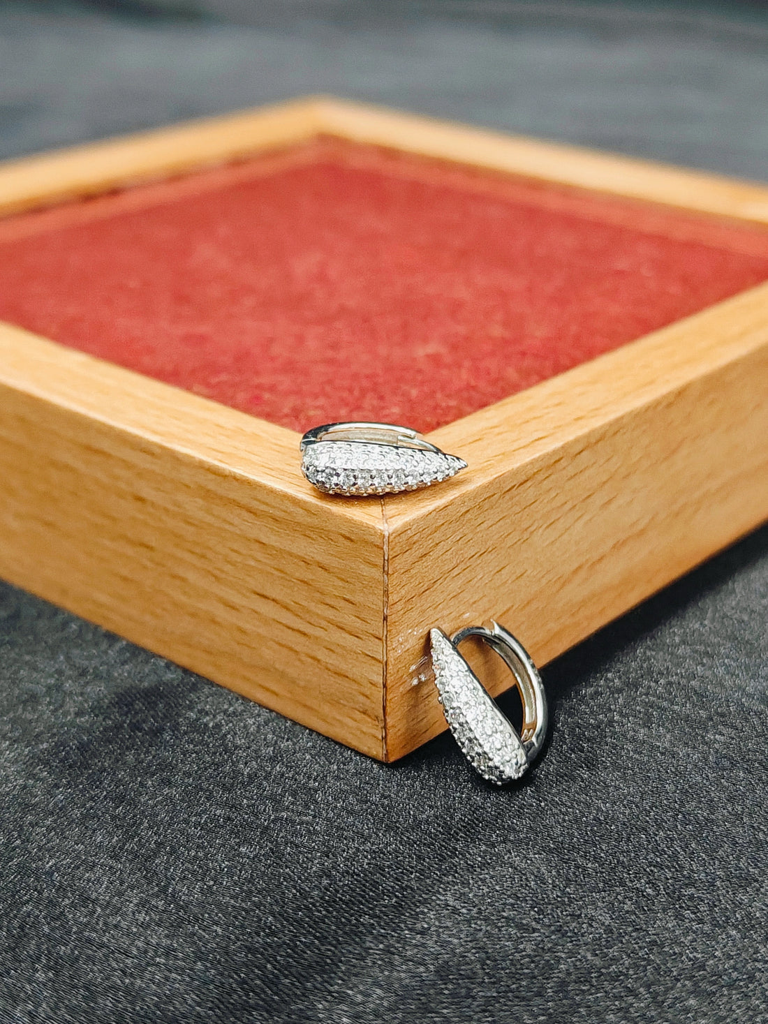 Two silver rings on a wooden jewelry box with red interior.
