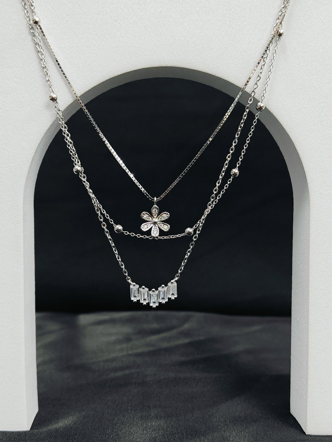 Layered silver necklaces with floral and bar pendants on a dark background