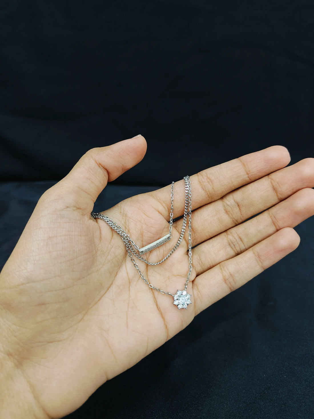 Hand holding two silver necklaces against a black background