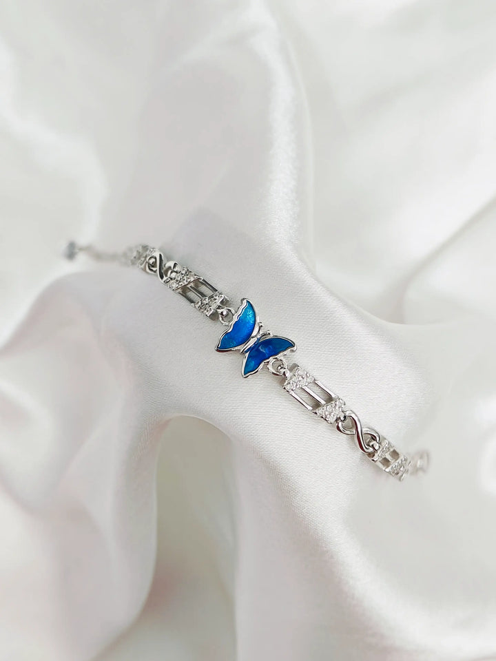 Silver bracelet with a blue butterfly charm on a white fabric background
