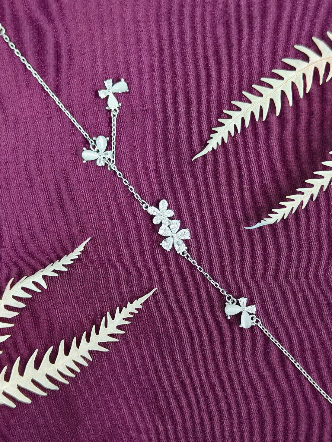Silver necklace with floral pendants on a purple fabric background