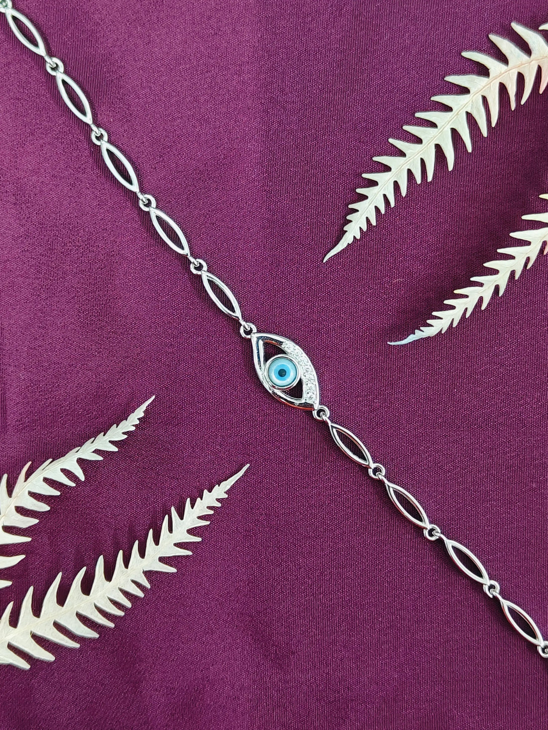 Silver chain necklace with an eye-shaped pendant on a purple fabric background