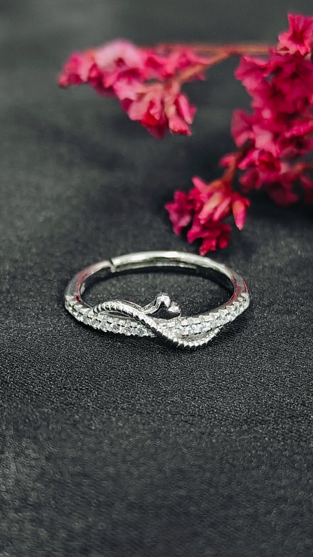 Silver ring with intricate design on a dark surface with pink flowers in the background