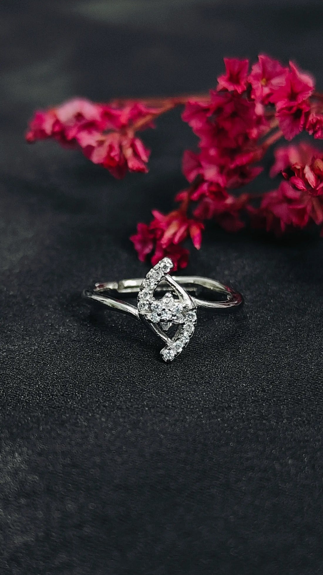 Silver ring with a decorative design on a dark surface with pink flowers in the background