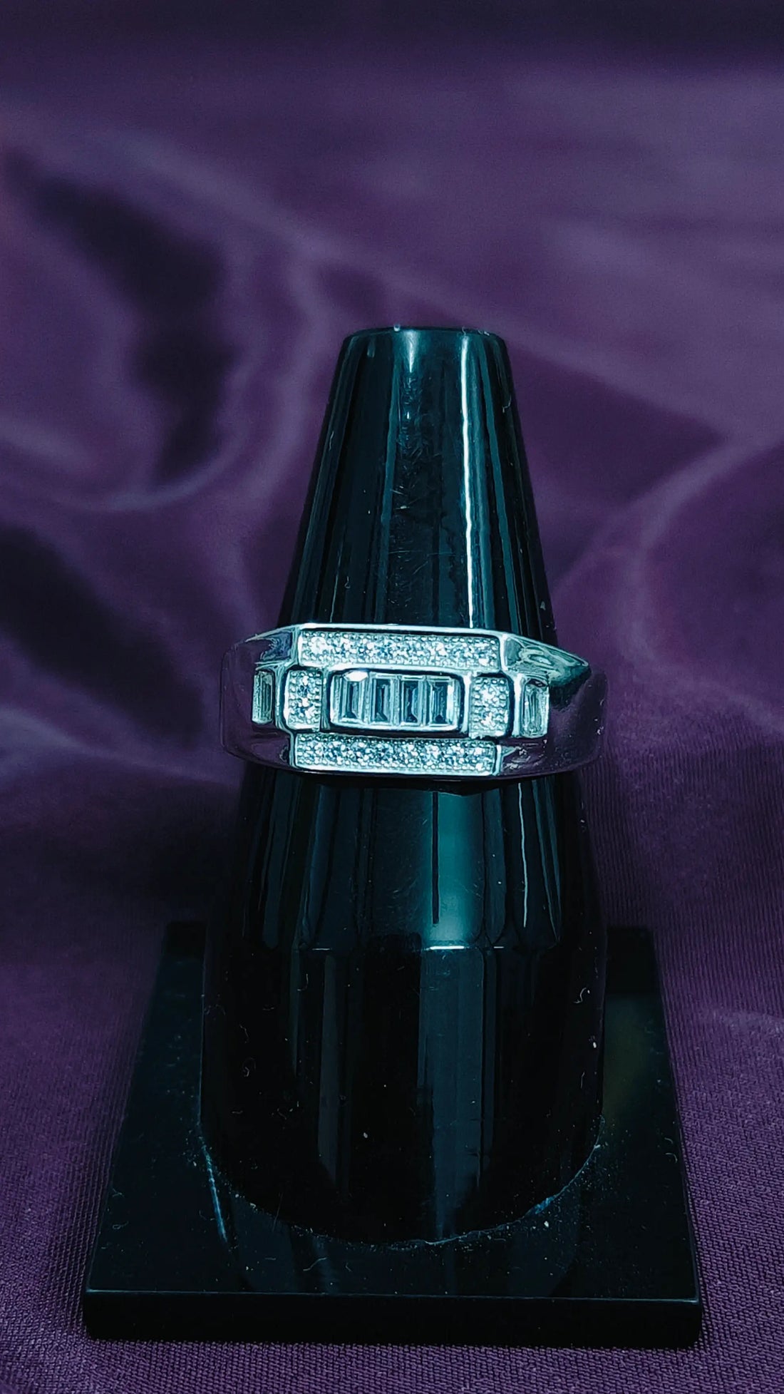 Silver ring with gemstones on a black stand against a purple fabric background