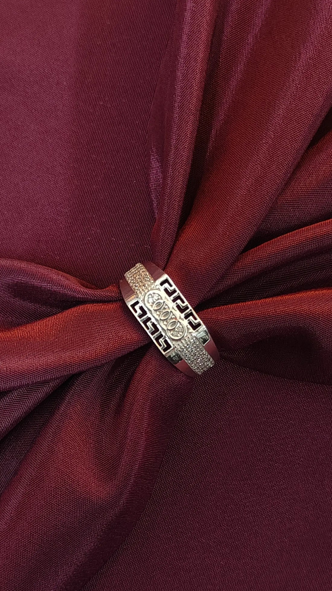 Silver ring with intricate design on a red fabric background