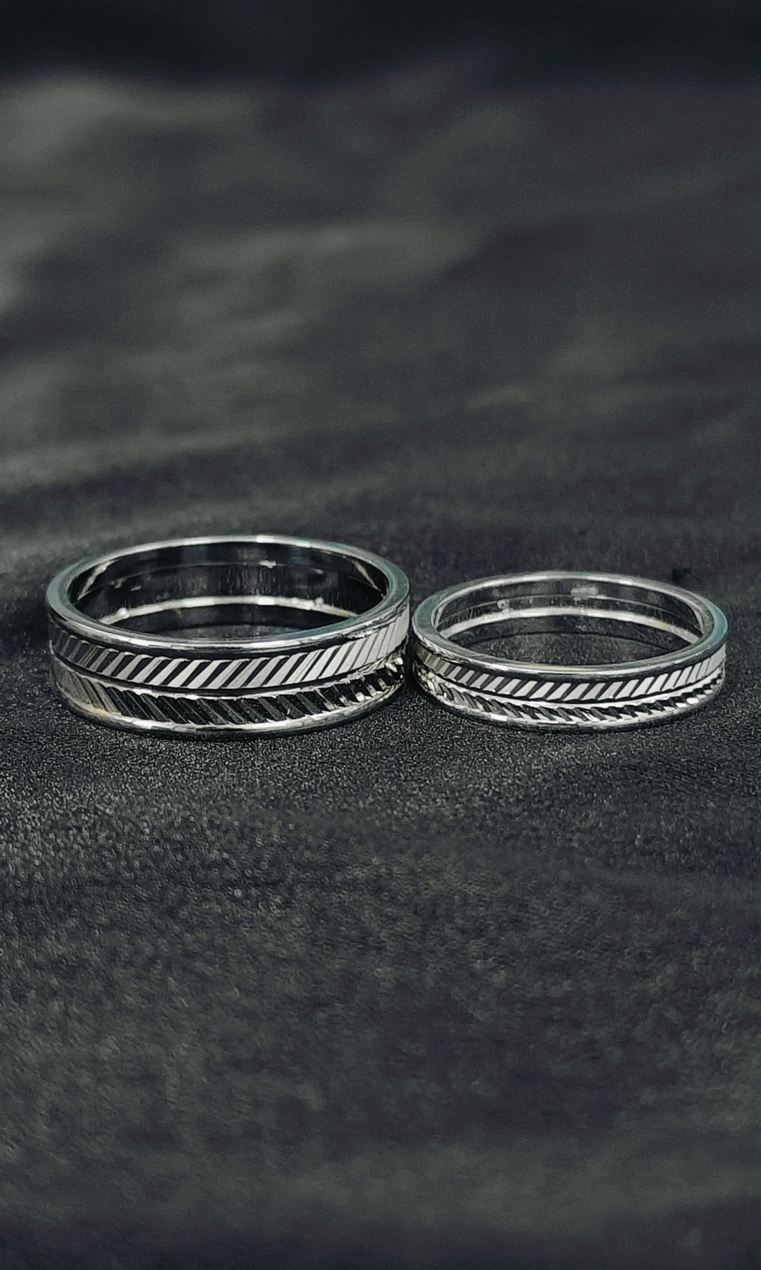 Two silver rings with textured designs on a dark textured surface