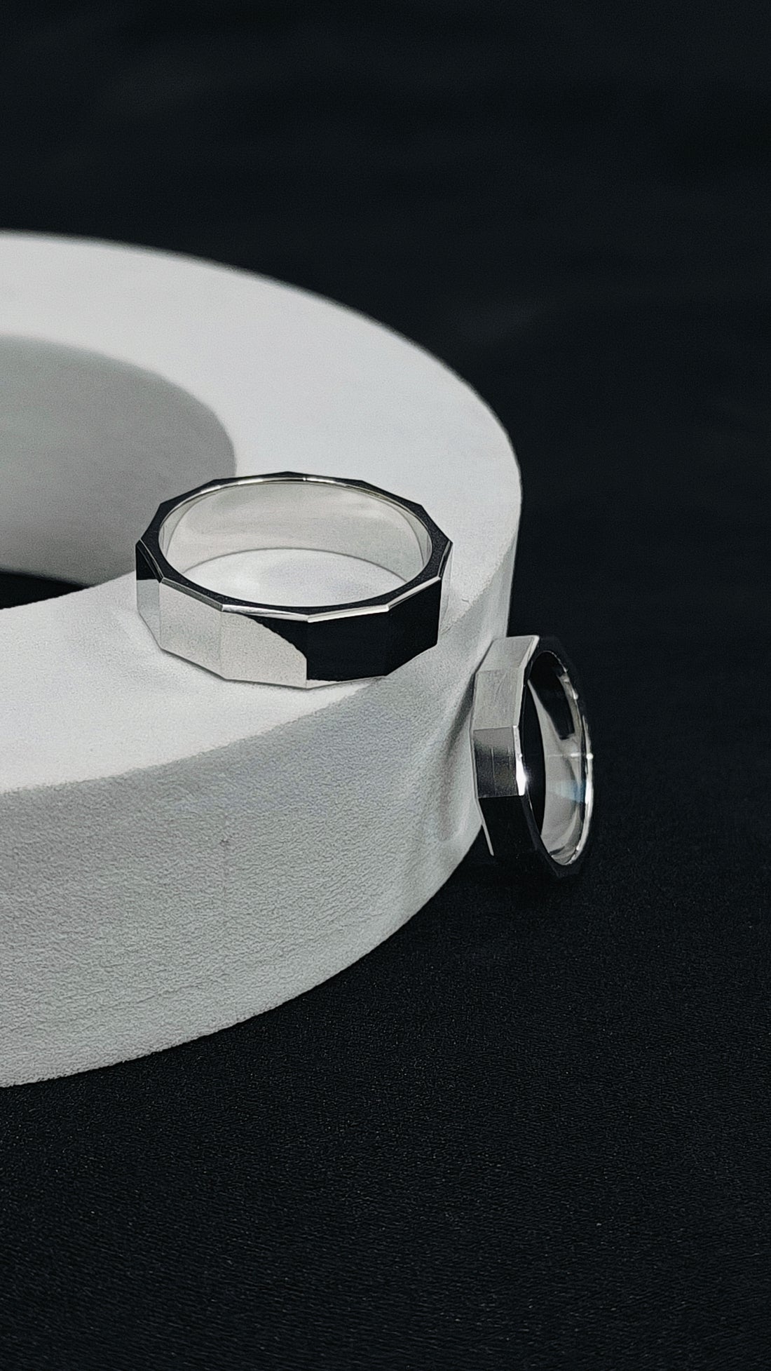 Silver ring with geometric design on a white cylindrical object against a black background