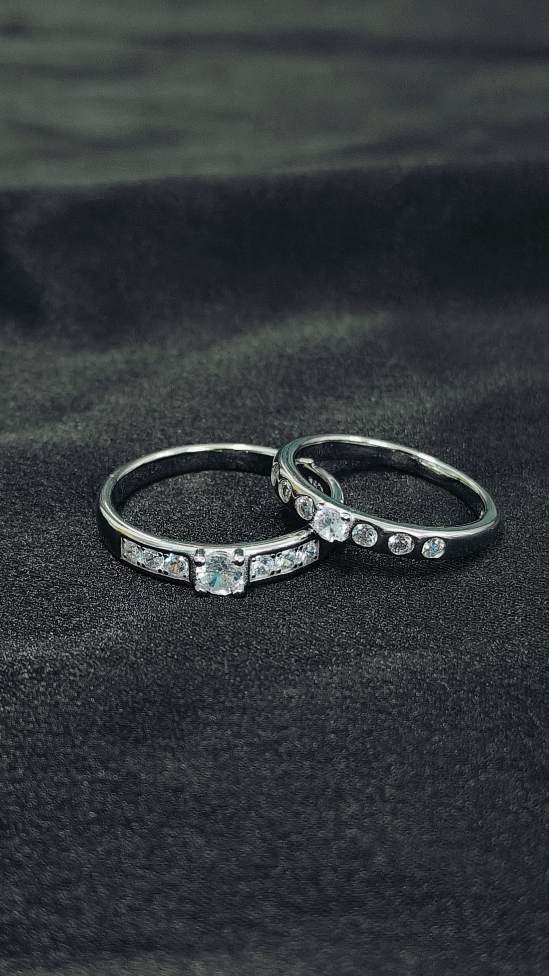 Two silver rings with gemstones on a black fabric background