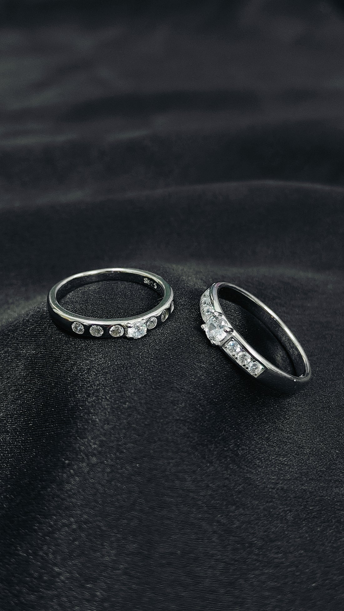Two silver rings with gemstones on a black fabric background