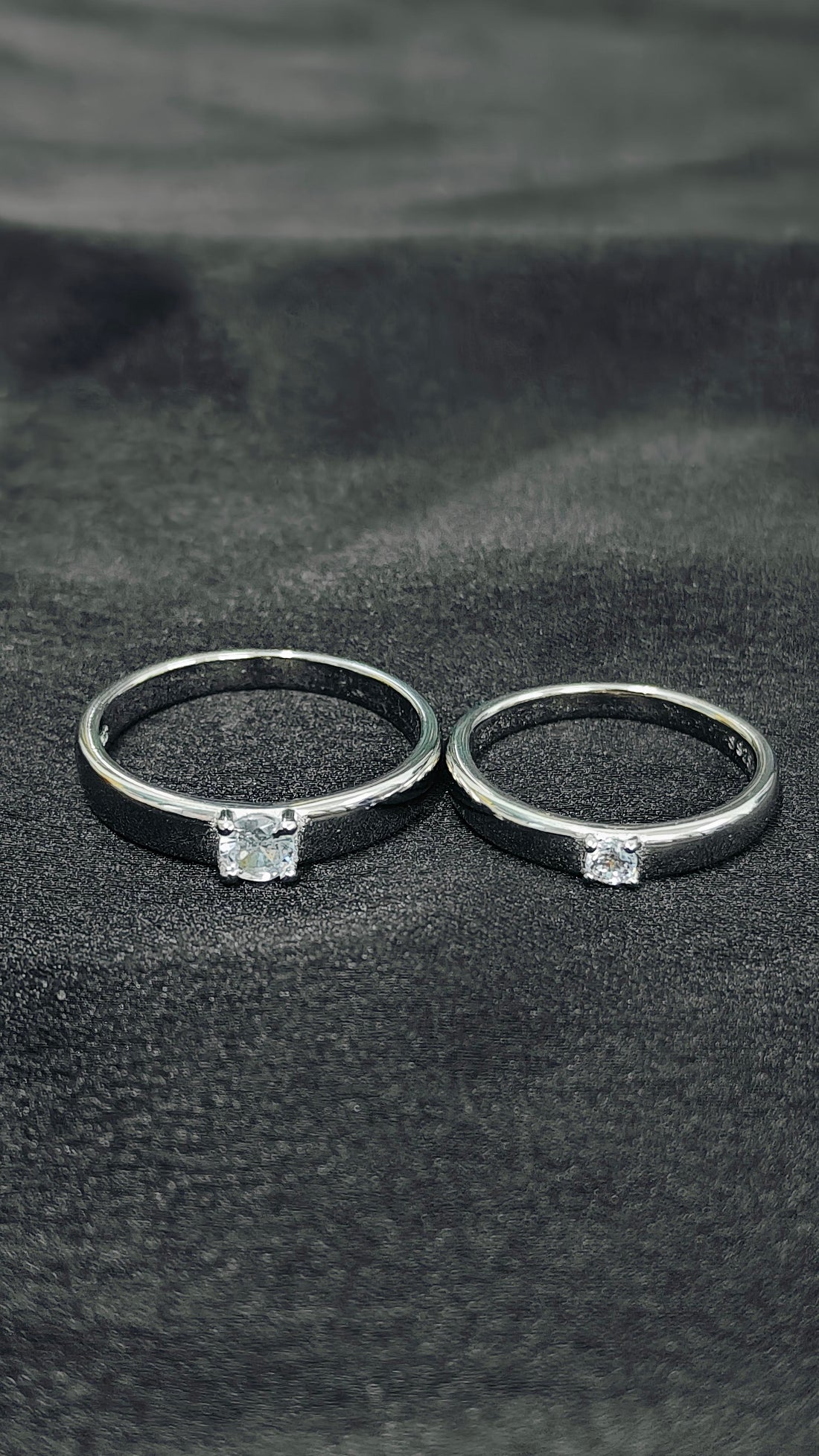 Two blackened silver rings with embedded diamonds on a dark fabric background