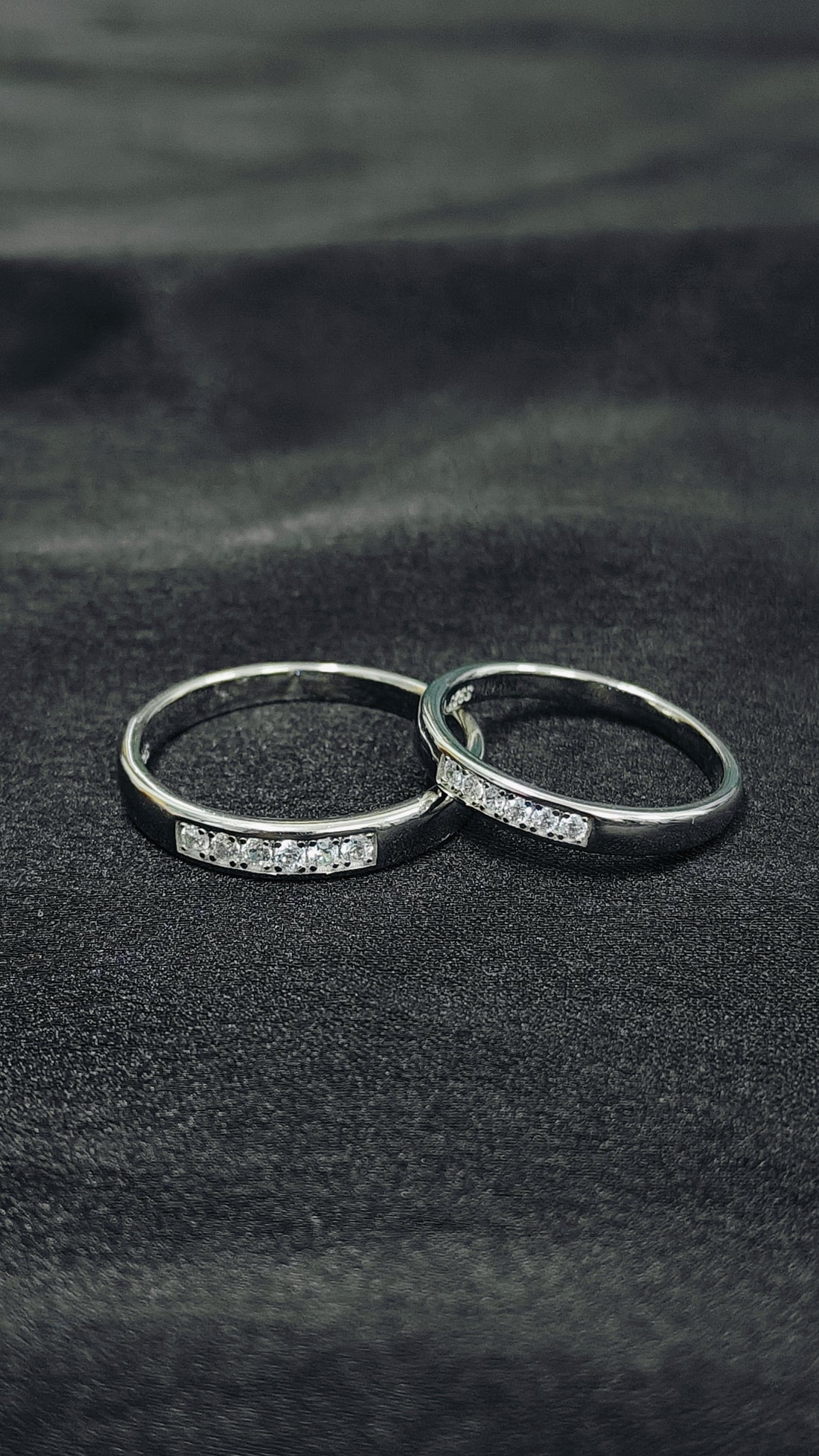 Two silver rings with small diamonds on a dark fabric background