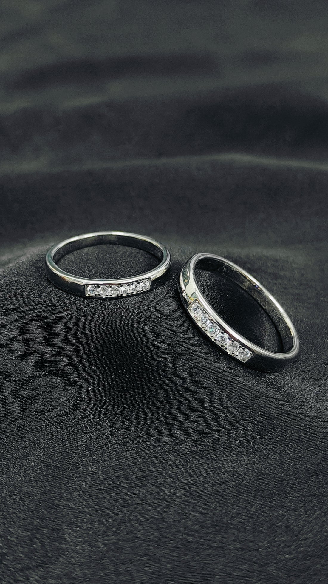 Two silver rings with embedded stones on a dark textured surface