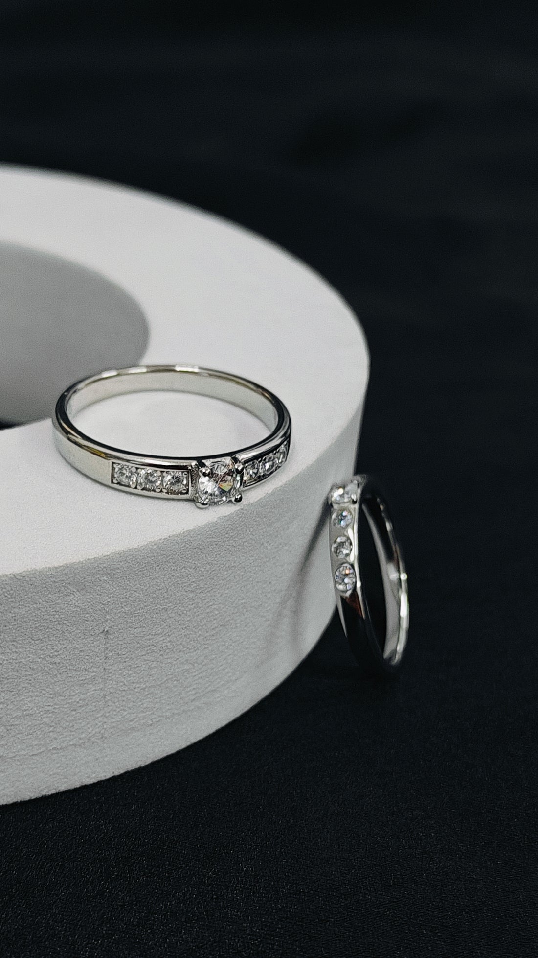 Silver ring with embedded diamonds on a white cylindrical object against a dark background