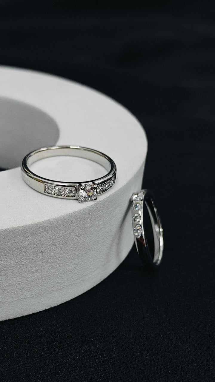 Silver ring with embedded diamonds on a white cylindrical object against a dark background