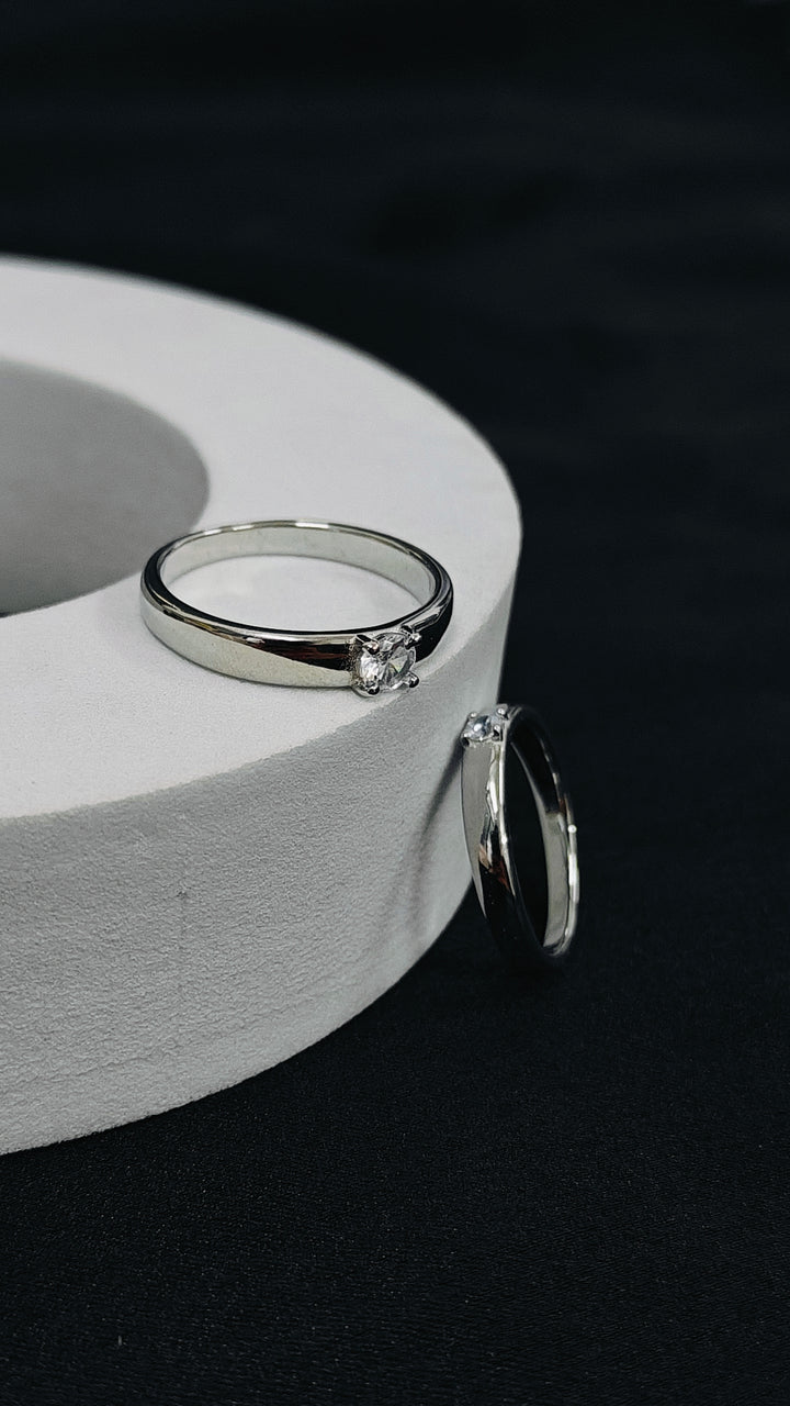 Silver ring with a diamond on a white cylindrical stand against a black background