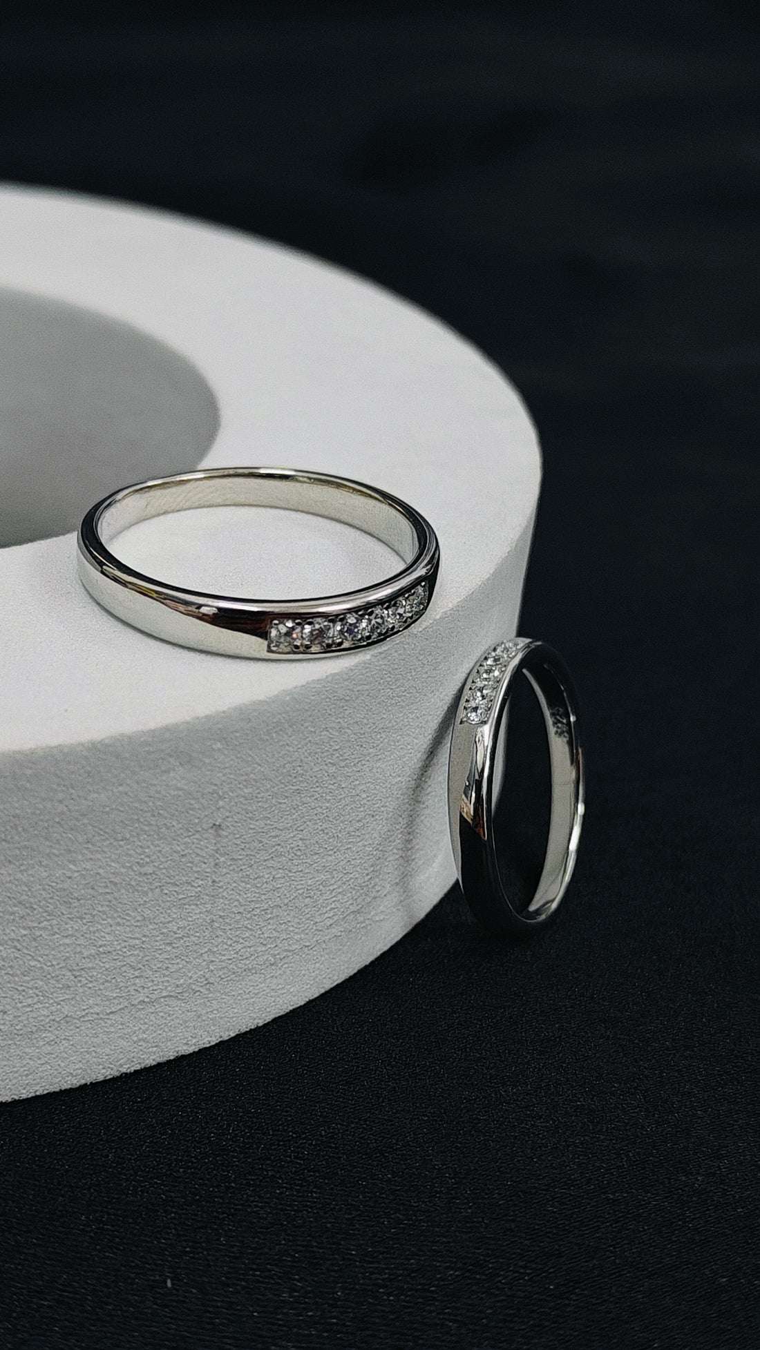 Two silver rings with gemstones on a white circular stand against a dark background