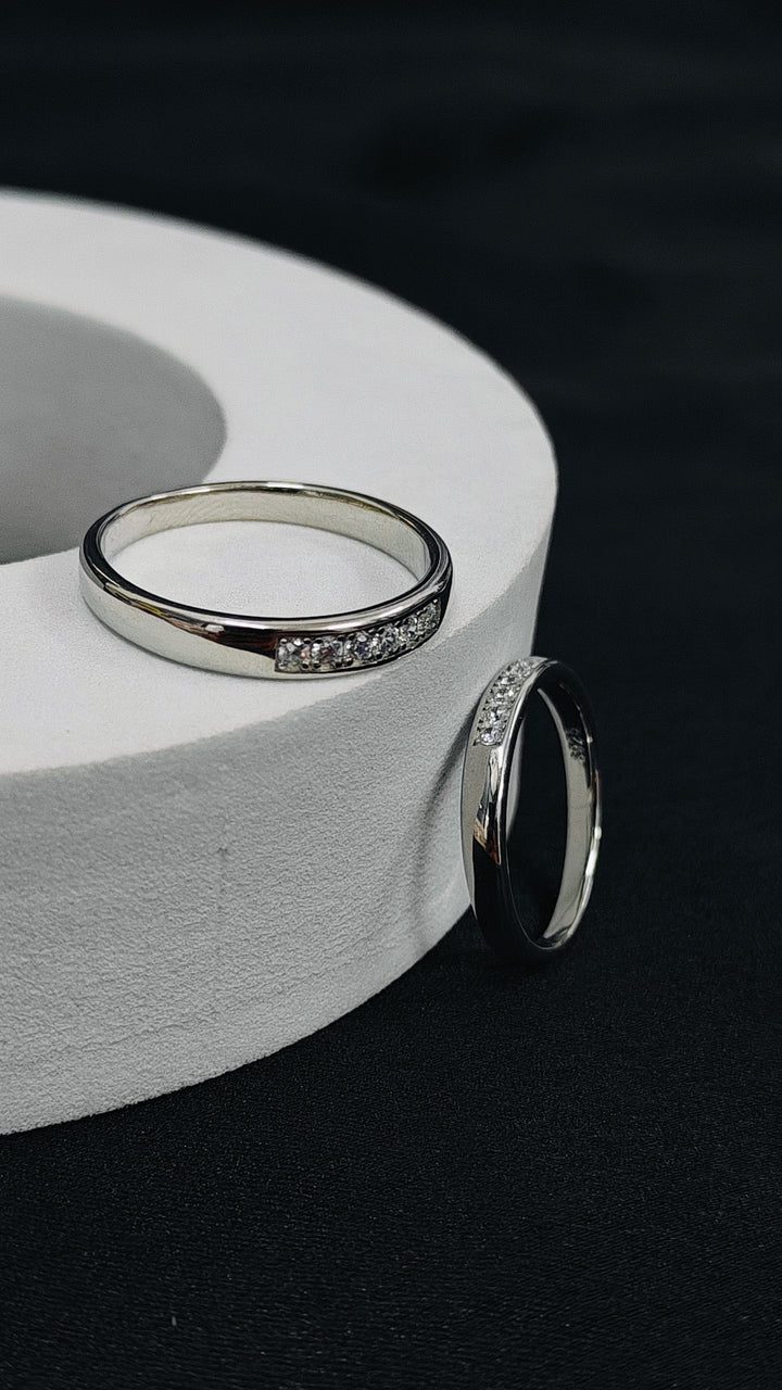 Two silver rings with gemstones on a white circular stand against a dark background