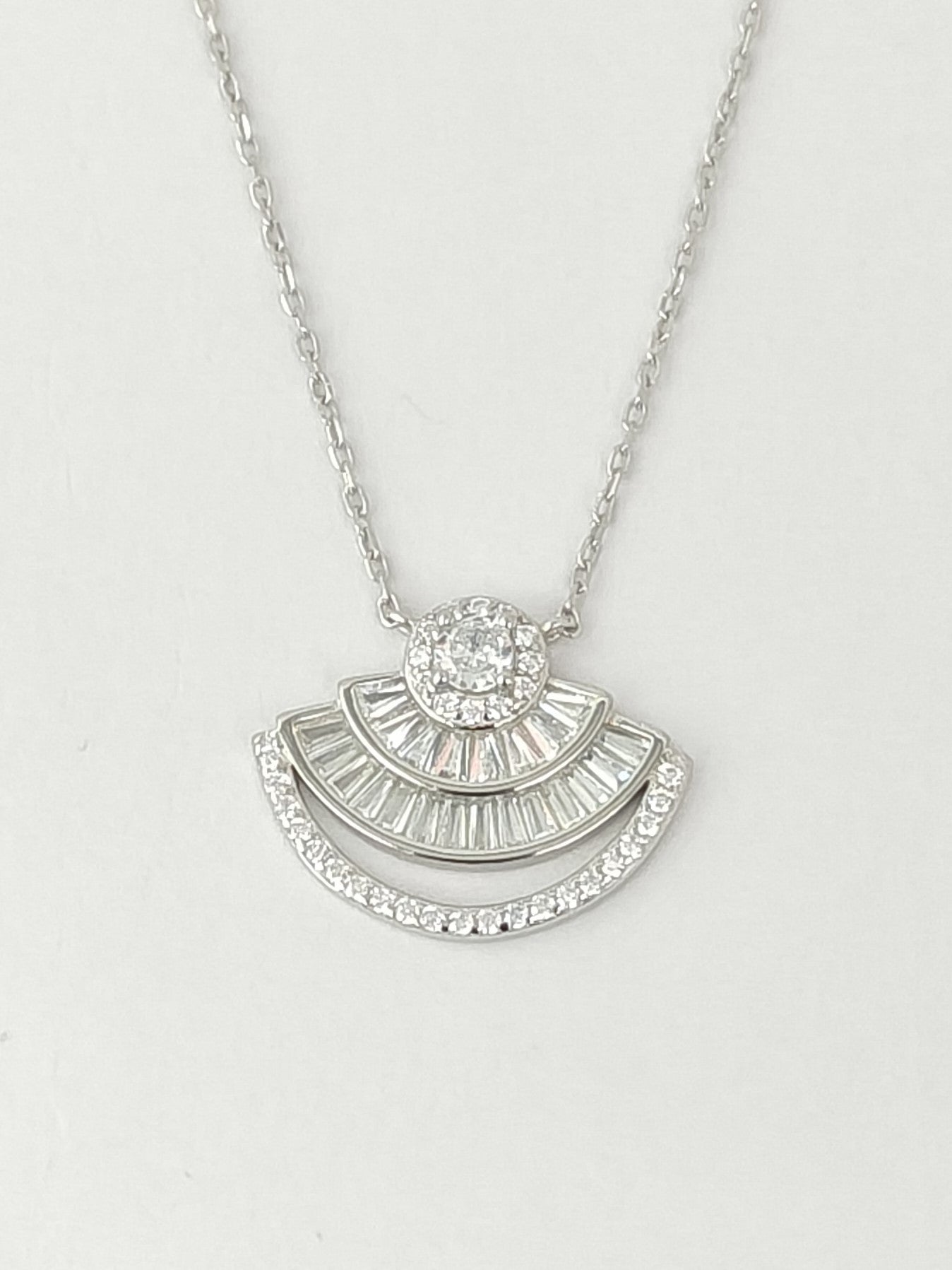 Silver necklace with a fan-shaped pendant on a light gray background