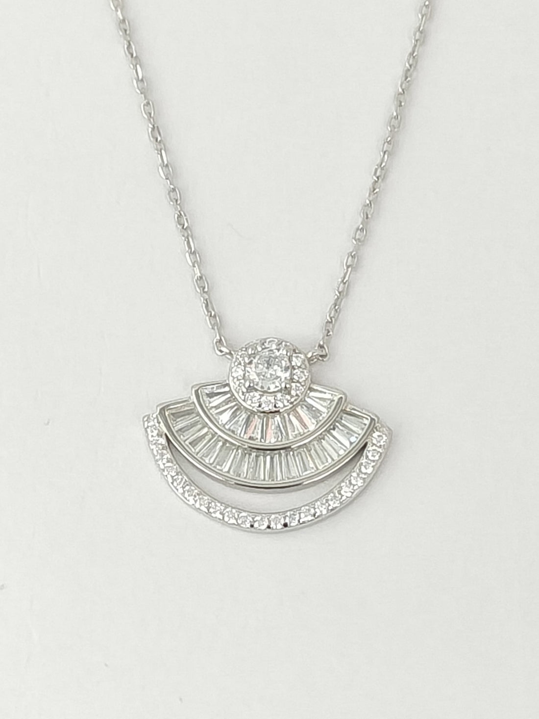 Silver necklace with a fan-shaped pendant on a light gray background