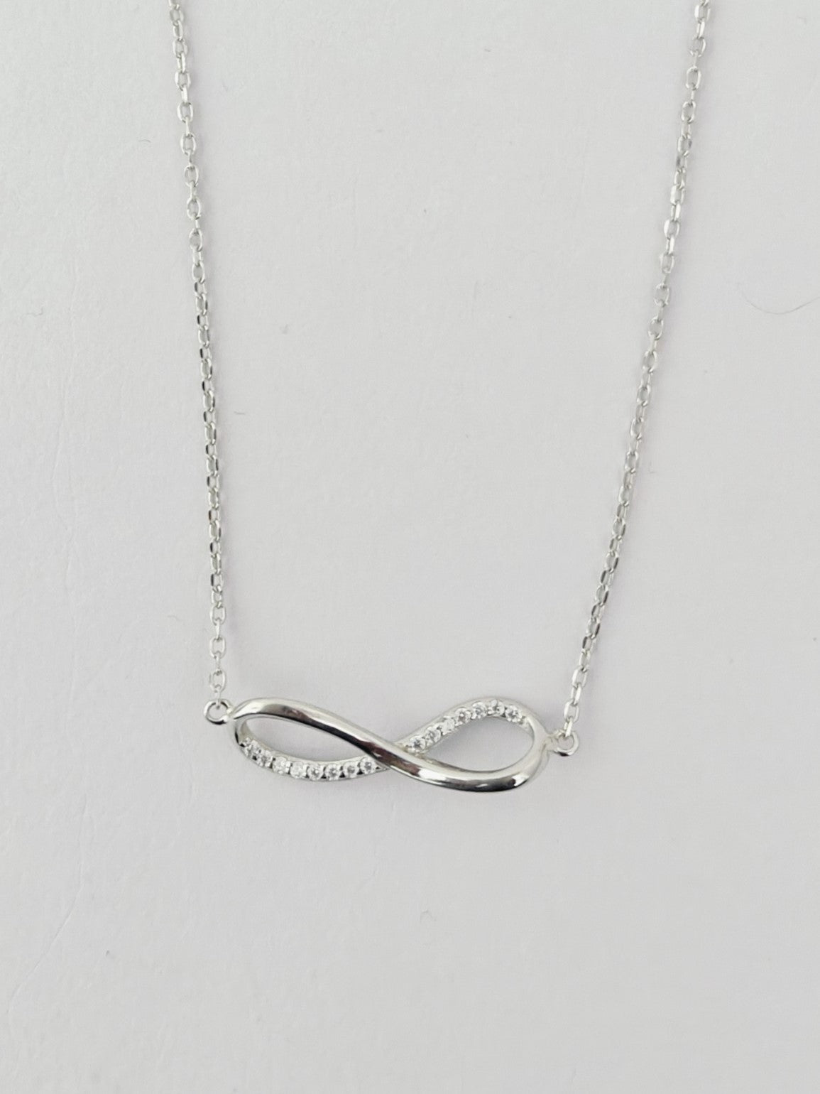 Silver infinity necklace on a light gray background